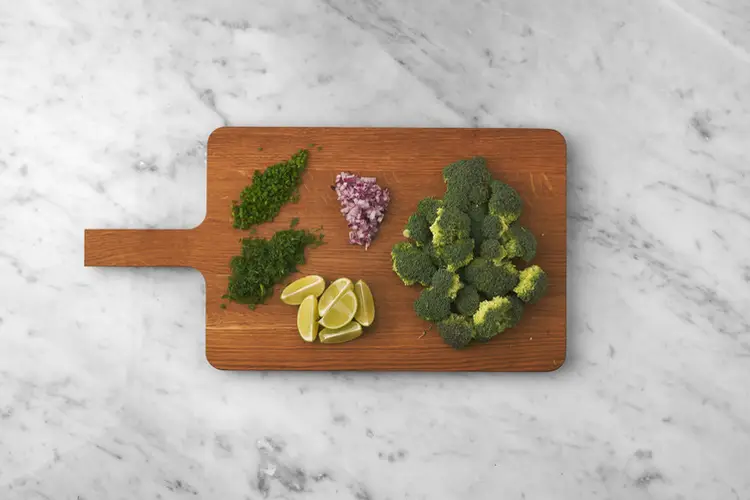 Frische Brokkoliröschen, fein gewürfelte rote Zwiebel, gehackter Dill und Zitronenspalten als vorbereitete Zutaten für einen proteinreichen Perlencouscous-Tuna-Salat.