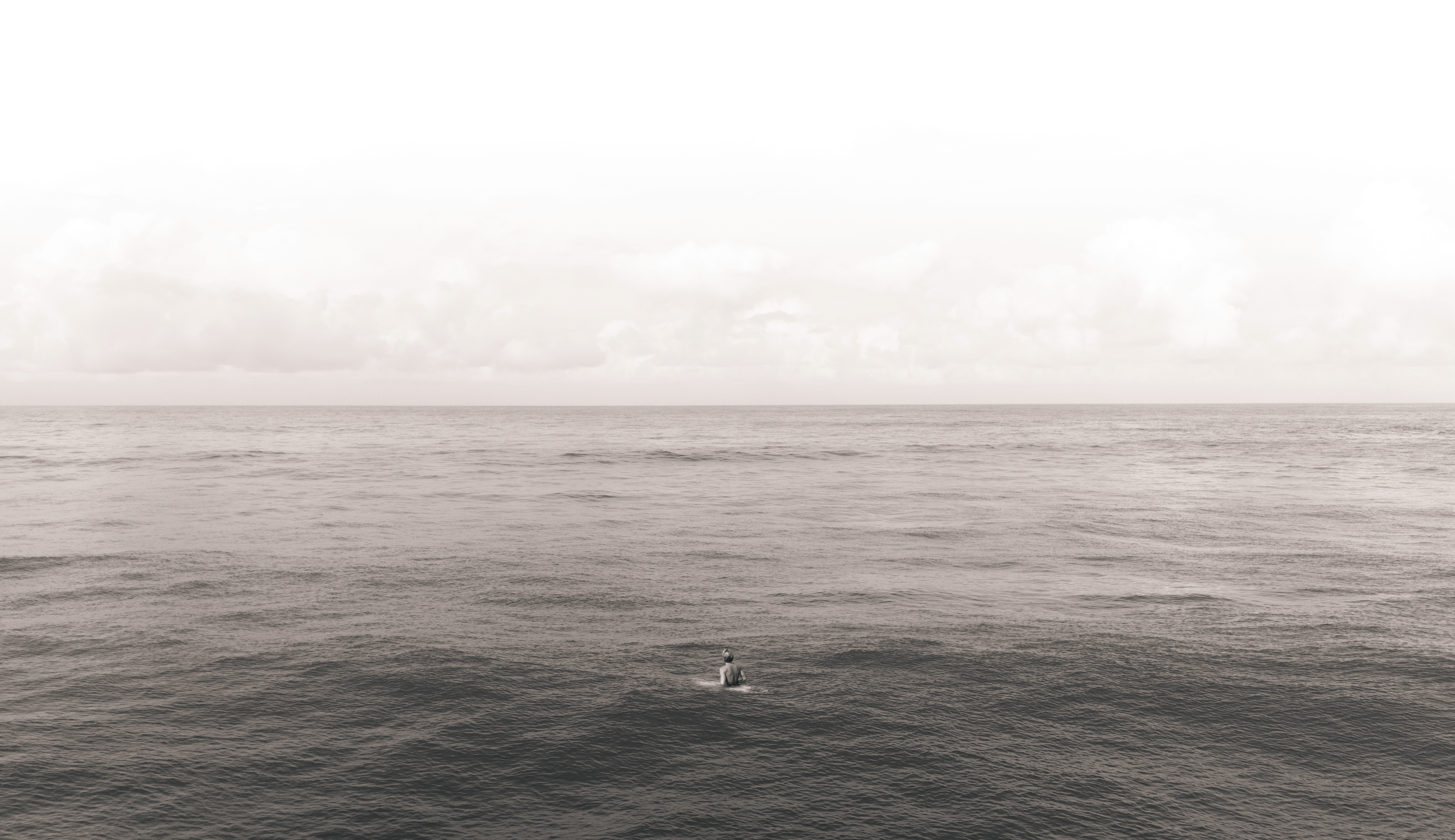Surfer sitting on a board in open water beneath a cloudy sky.
