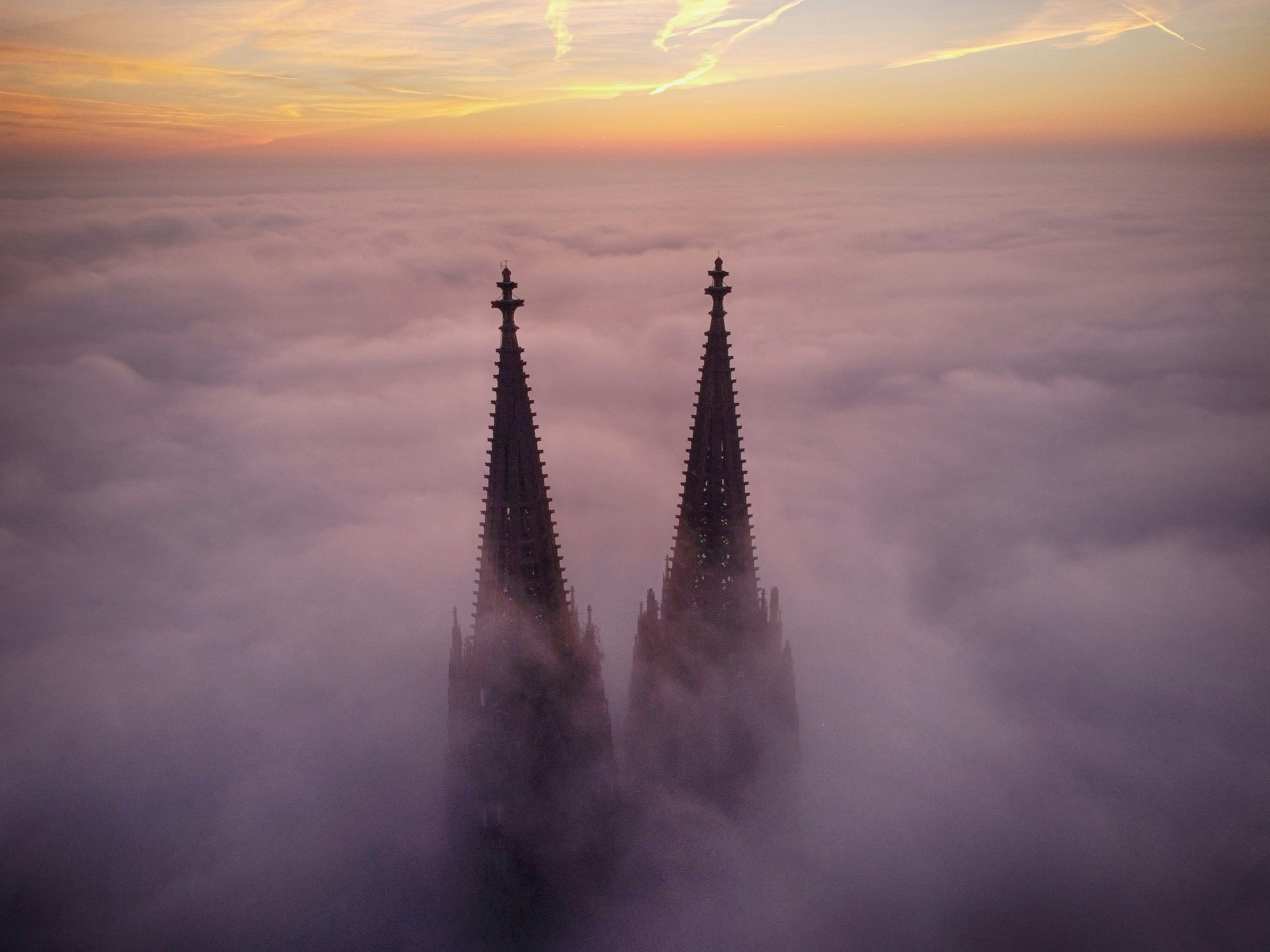 Two spires emerge from a sea of clouds at sunset.