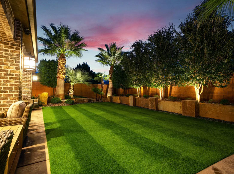 This is a picture of an inviting backyard at sunset adorned with lush artificial AGL Grass and softly glowing lights, creating a cozy ambiance.