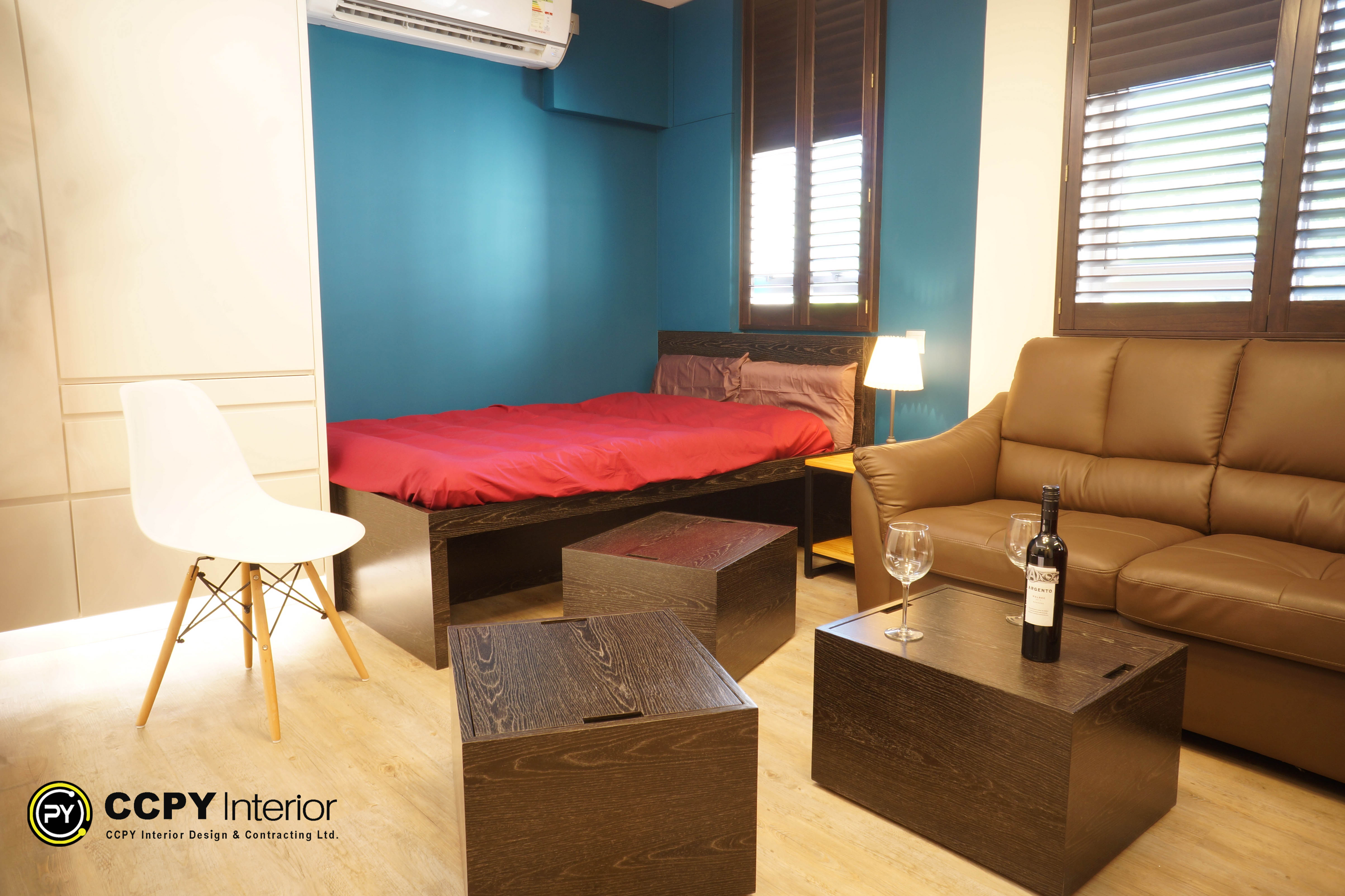 The selected region shows an interior view of a compact apartment designed with a "Smart Luxury" theme to optimize a 380-square-foot floor area.Key Layout & Furniture ElementsMultifunctional Living Area: The space combines a sleeping zone and a seating area into a single, cohesive room layout.Platform Bed: A dark wood platform bed frame with a contrasting red mattress cover sits against a teal accent wall.Seating & Social Space: A brown leather sofa is positioned adjacent to the bed, paired with two matching dark wood cubic side tables that double as coffee tables.Modern Accents: A white molded shell chair with light wood legs adds a contemporary touch to the flooring area.Natural Lighting: Large windows with horizontal blinds allow controllable natural light to brighten the wood-floored interior.