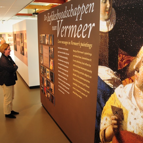 A person observes an exhibit panel titled "De liefdesboodschappen van Vermeer" with information and images about Vermeer's paintings.