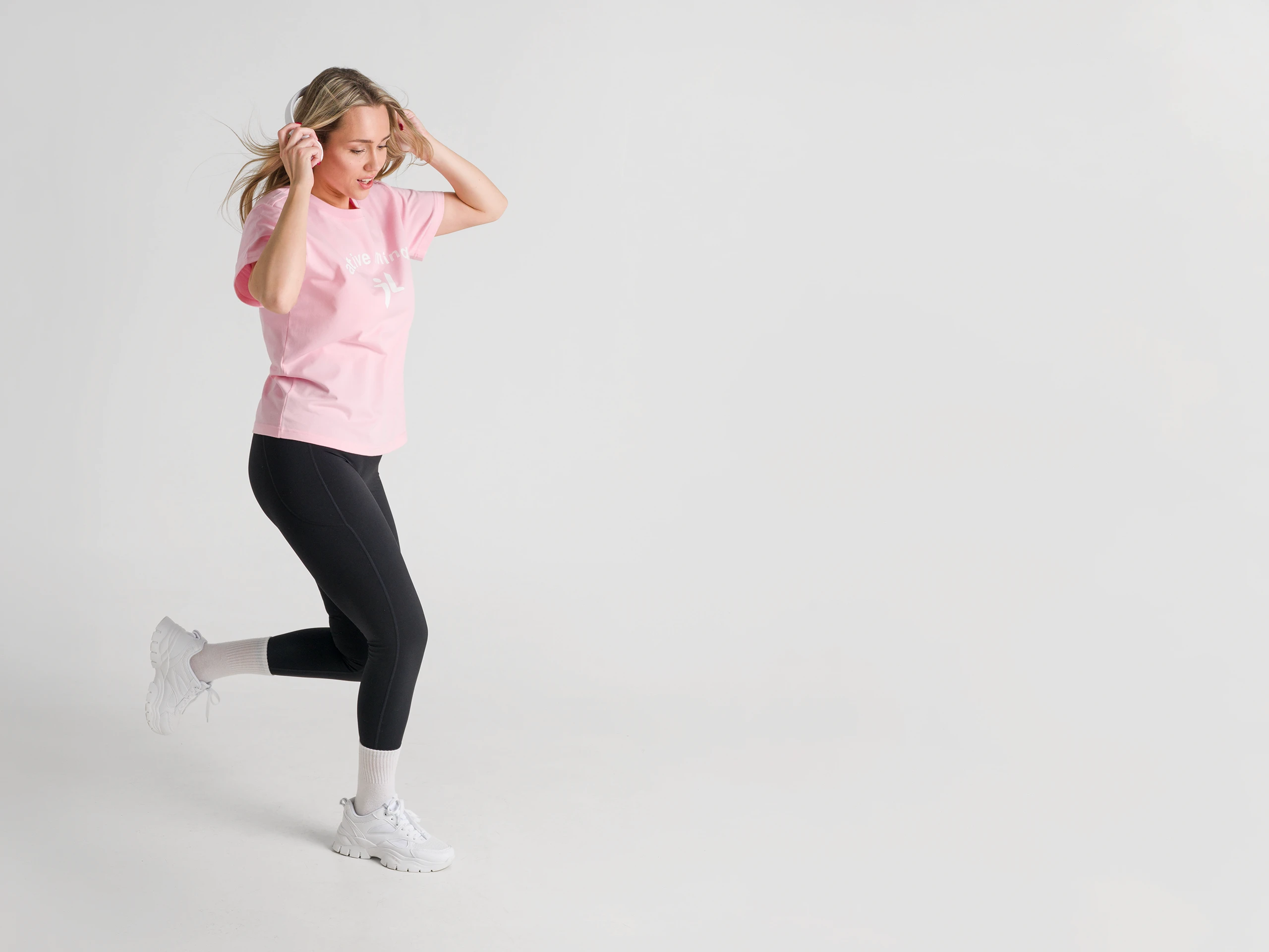 Female athlete in a pink t-shirt and black leggings, moving in a studio.