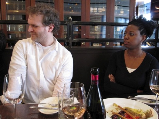 A photo of two people sitting at a restaurant table and listening to someone.