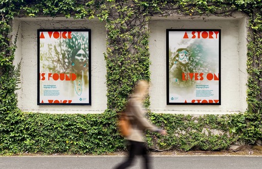 Woman walking past two large, cyanotype posters on a vine-covered wall.