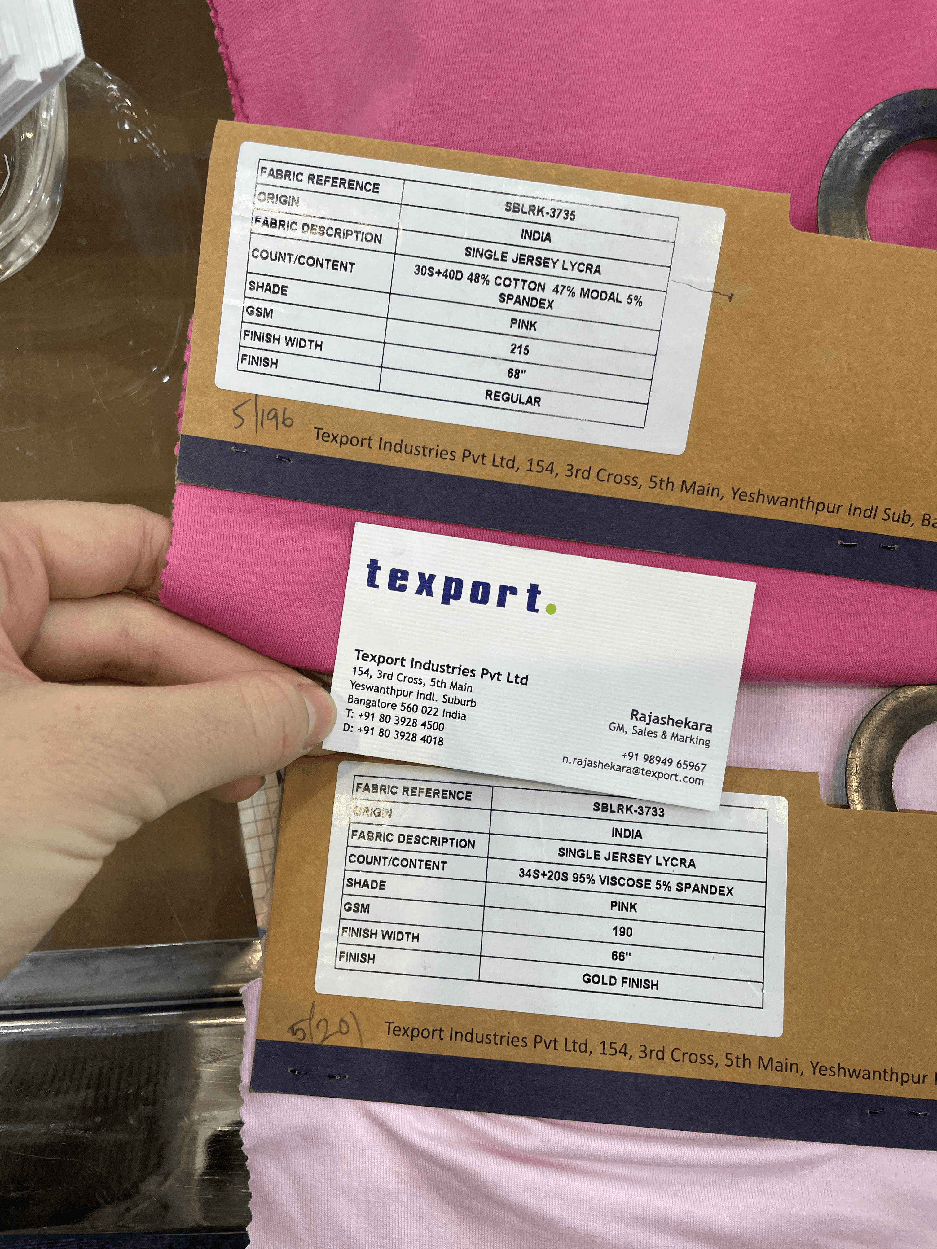 Close-up of two pink textile samples with manufacturer labels detailing fabric content, weight, and finish.