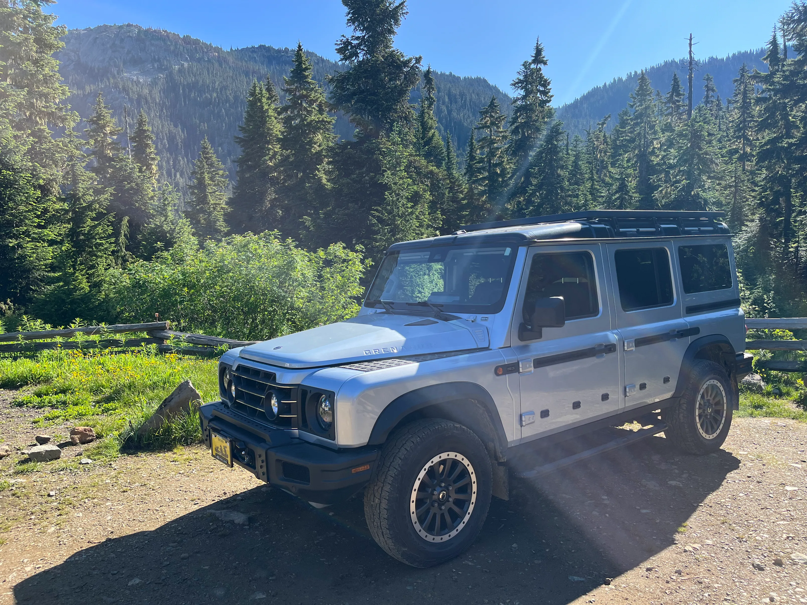 White INEOS Grenadier off-road SUV parked in a scenic mountain forest during a sunny overlanding adventure
