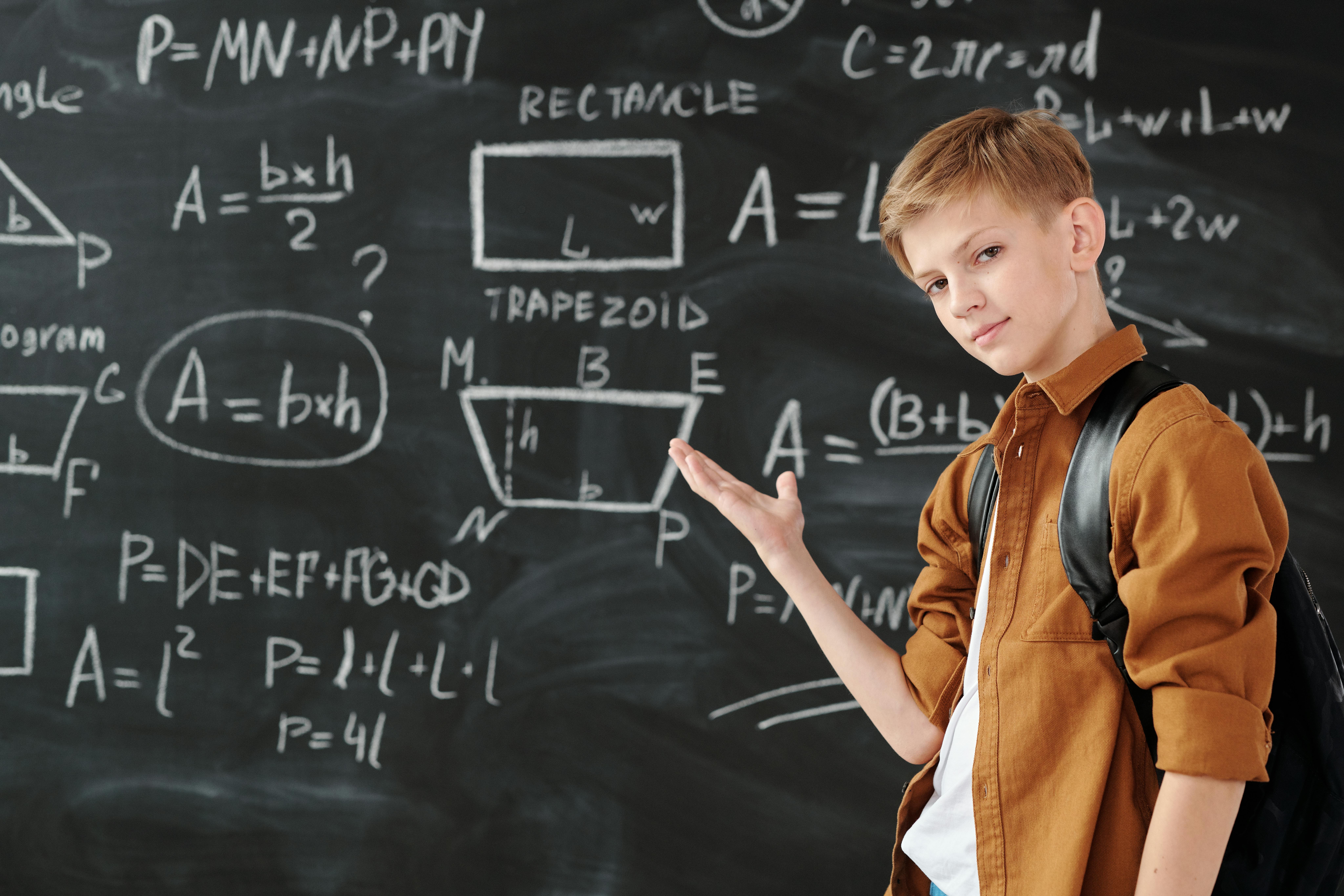 Boy in Brown Jacket Standing in Front of Chalk Board with symbols and letters