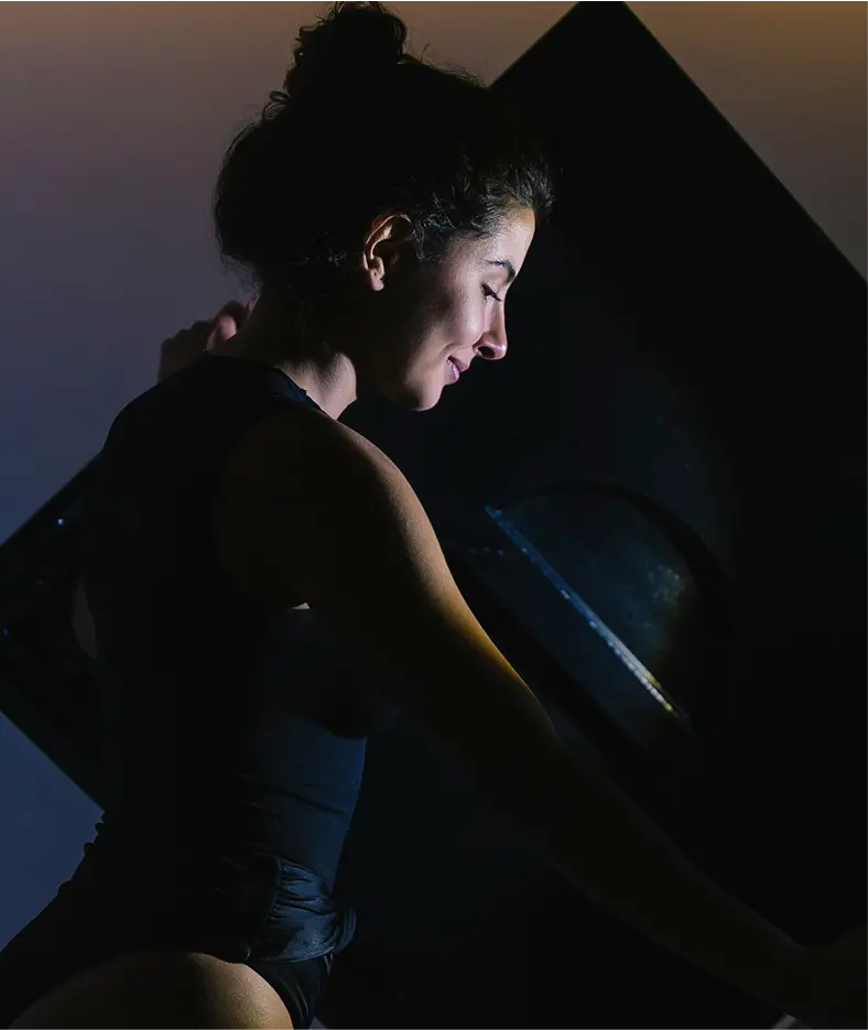 A person in a dark, serene environment is illuminated by soft lighting, exuding a sense of calm and focus, embodying the essence of premium fitness, spa, and wellness retreats.