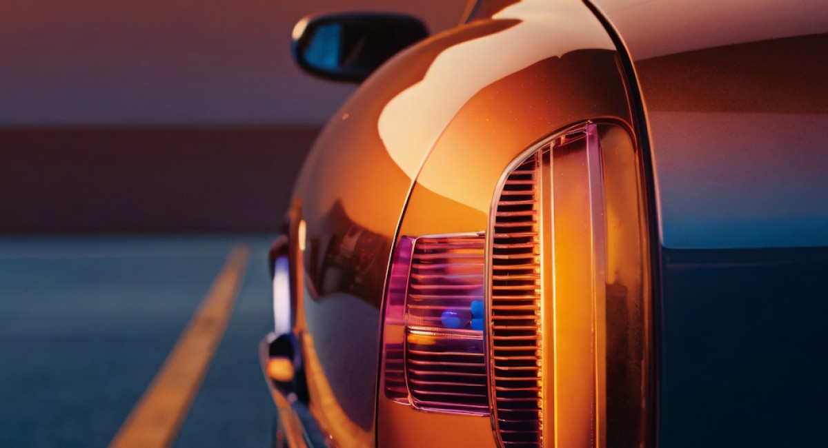 Close-up of a car's rear light reflecting sunset colors on a road with horizon