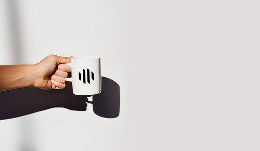 Hand holding a coffee mug with Heads logo