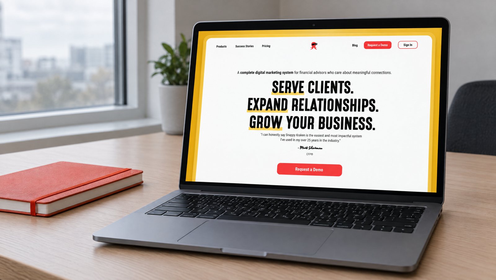 A laptop on an office desk showing the real Snappy Kraken homepage designed by Demand Designer: 'Serve clients. Expand relationships. Grow your business.' with a Request a Demo button