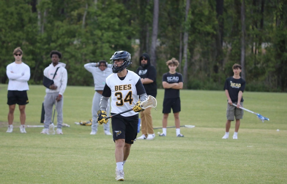 Lacrosse player jogging on field with people in the background