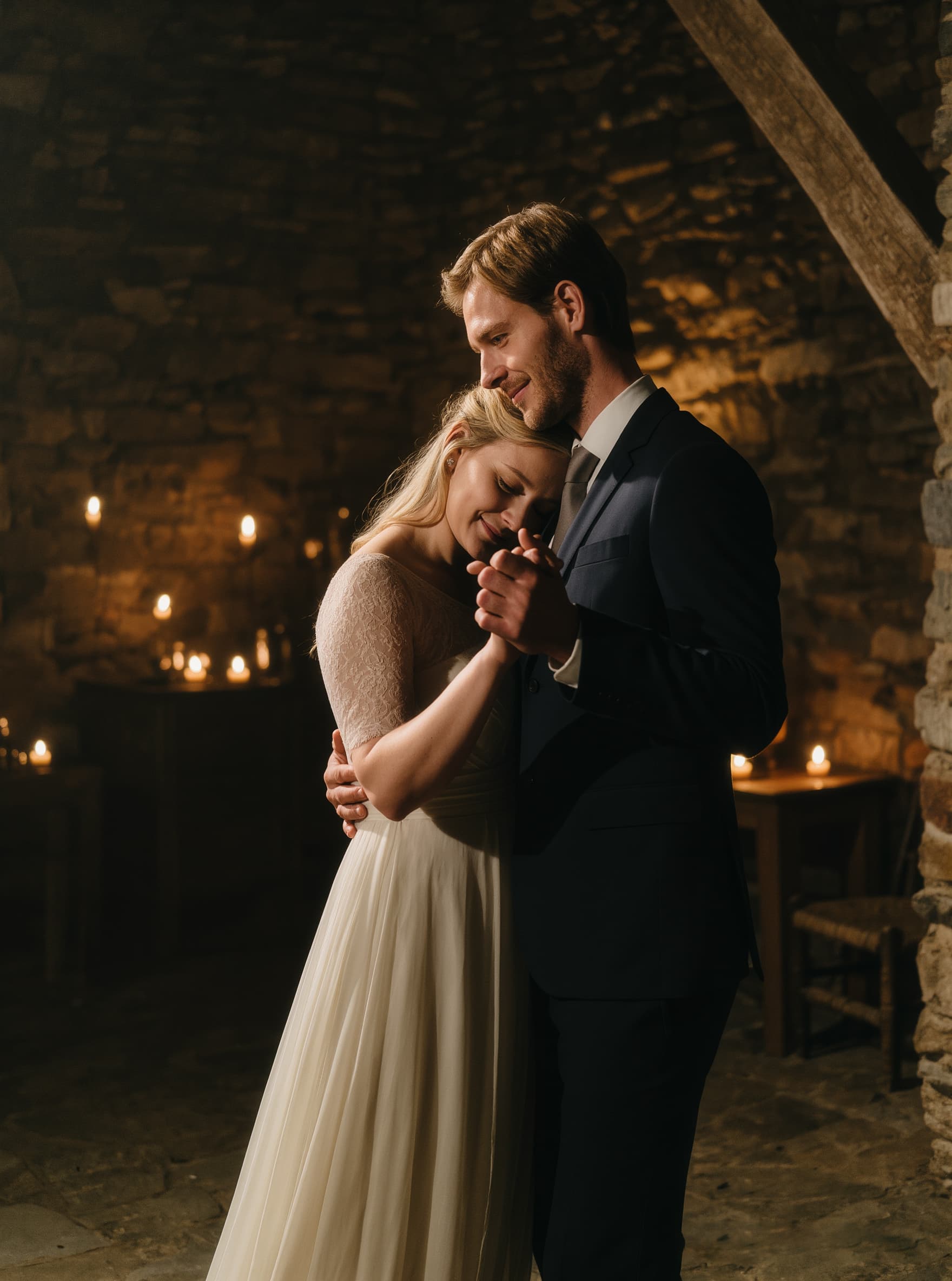 Wedding photo – couple embracing tenderly by candlelight in stone venue, The Cotswolds