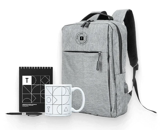 Uma mochila cinza ao lado de uma caneca de café e uma caixa pequena, sugerindo um cenário de viagem ou de escritório.