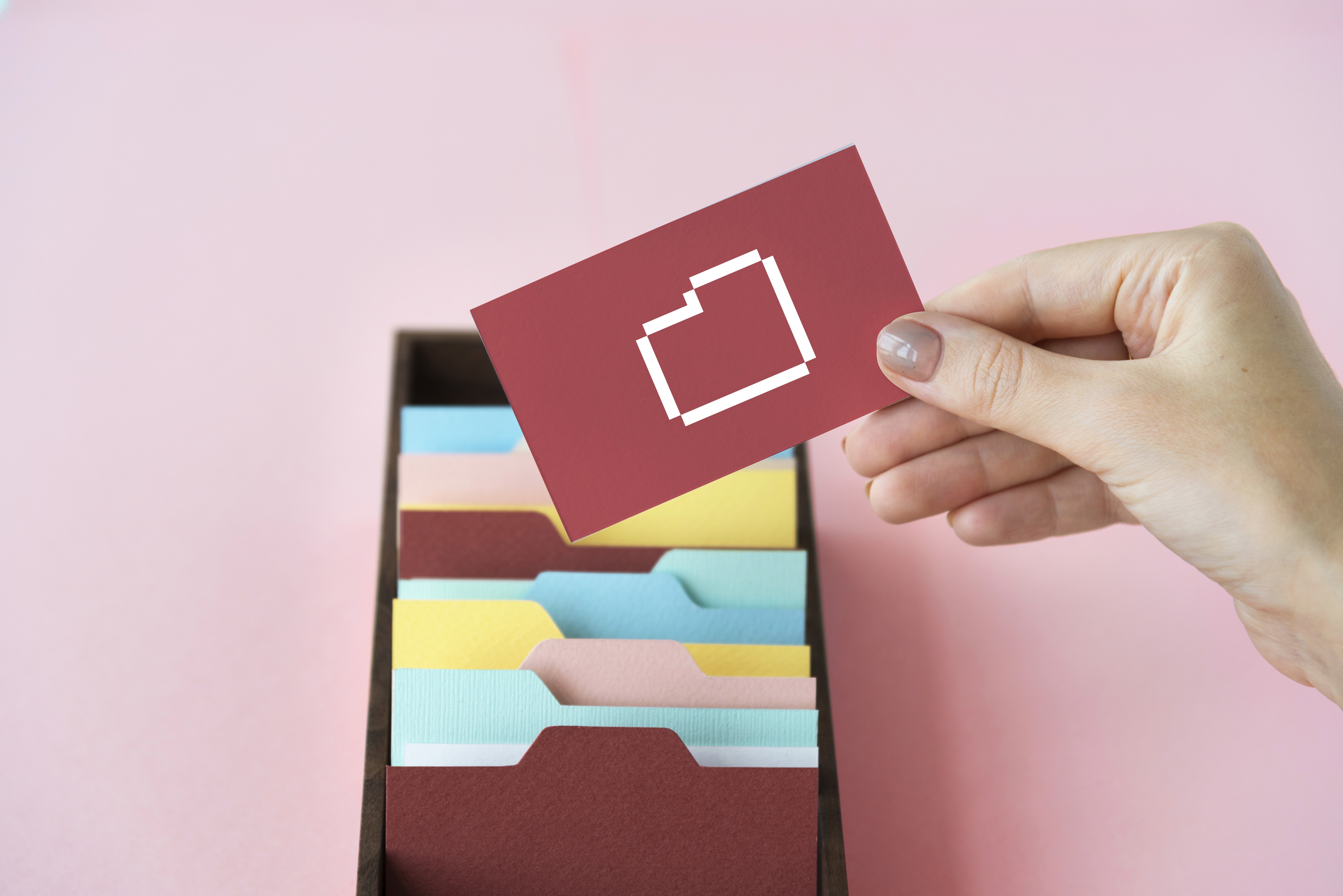 Female hand with a red card on a pink desk and a container of colourful postcards