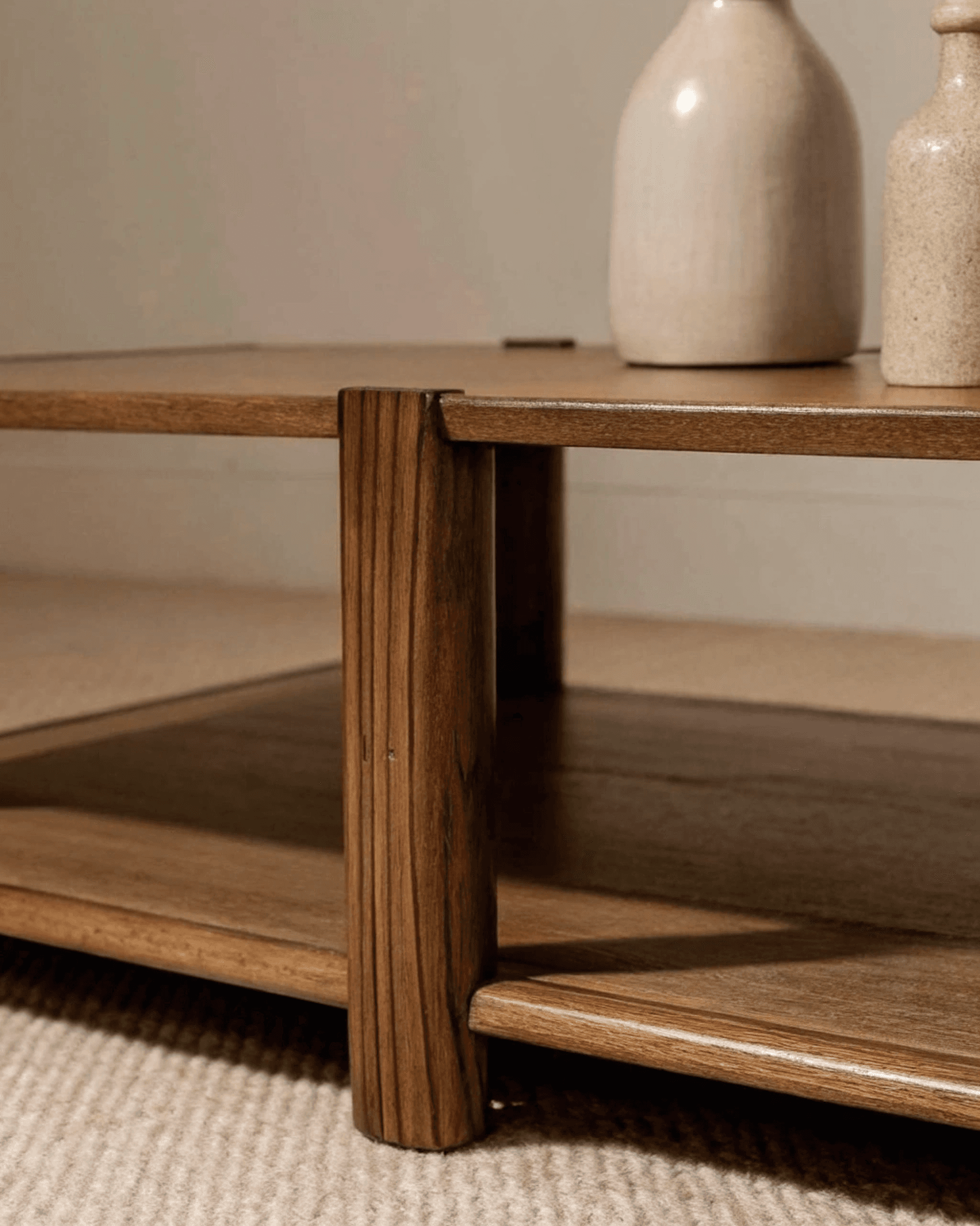 Minimalist wooden coffee table with rounded legs, a lower shelf, and neutral ceramic vases on top, set against a cozy beige backdrop.