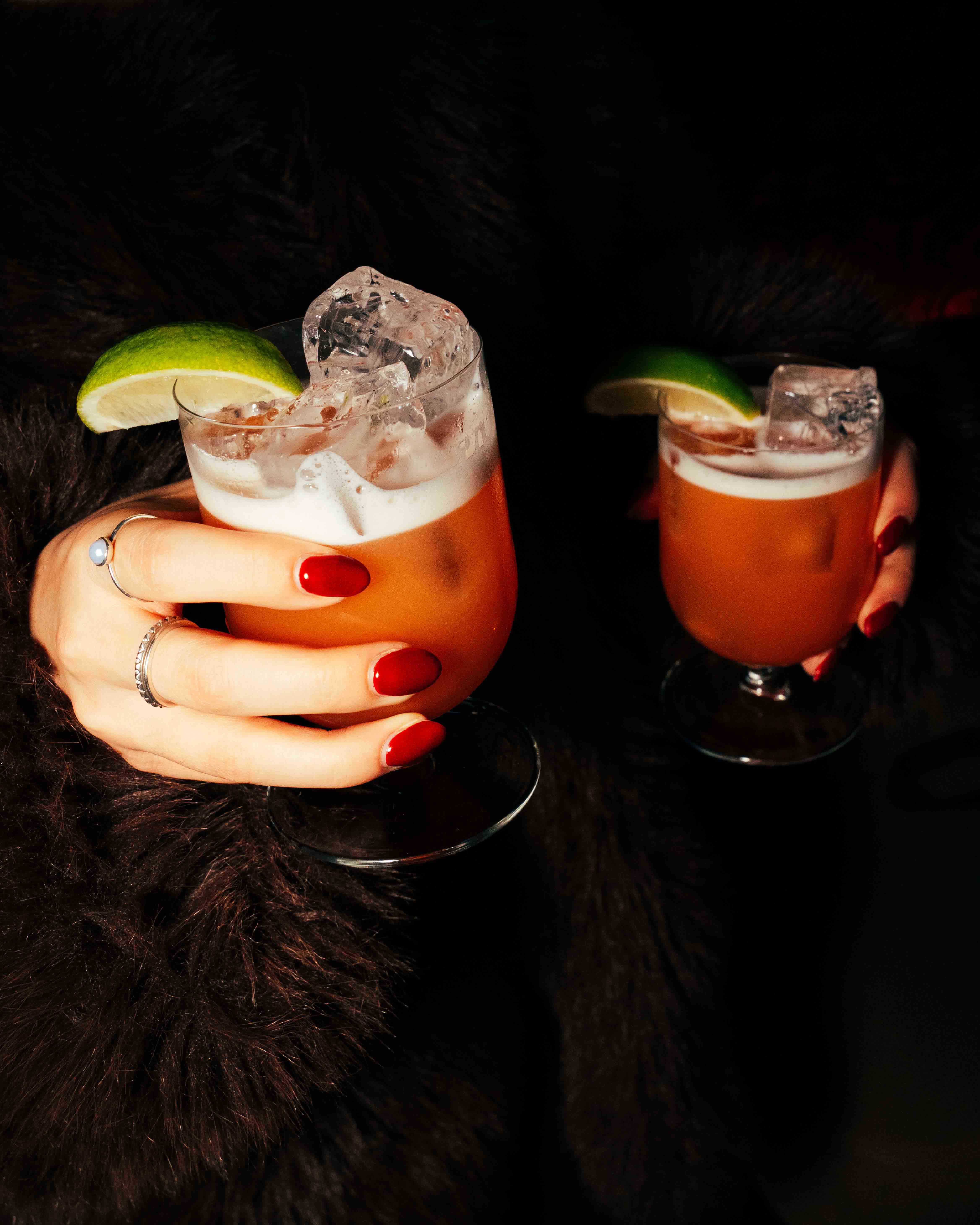 White plate with roasted carrots served on green sauce, topped with almonds and fresh herbs, held by a hand over a dark table.
