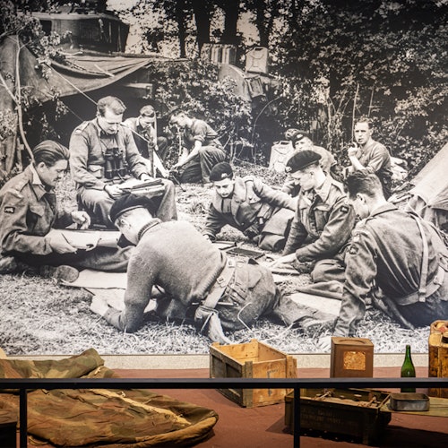 Ein Schwarz-Weiß-Foto von Soldaten in einer Campingszene, mit verschiedener Ausrüstung und Kisten im Vordergrund.