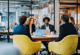 A diverse group of people collaborating around a table, discussing ideas and analyzing documents together.