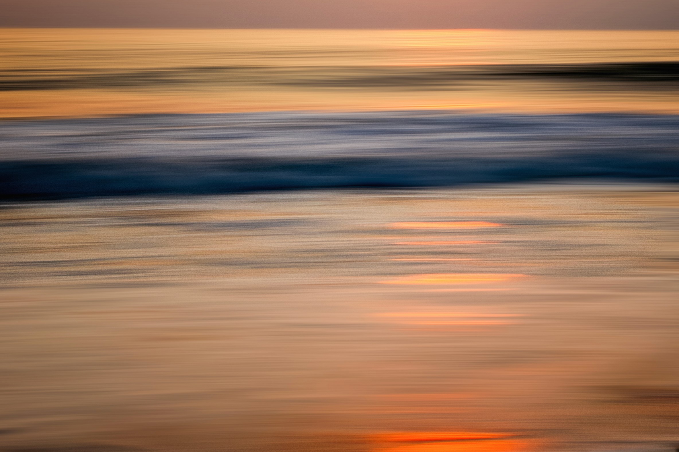 Waves and horizon blurred into soft copper and orange tones at dusk