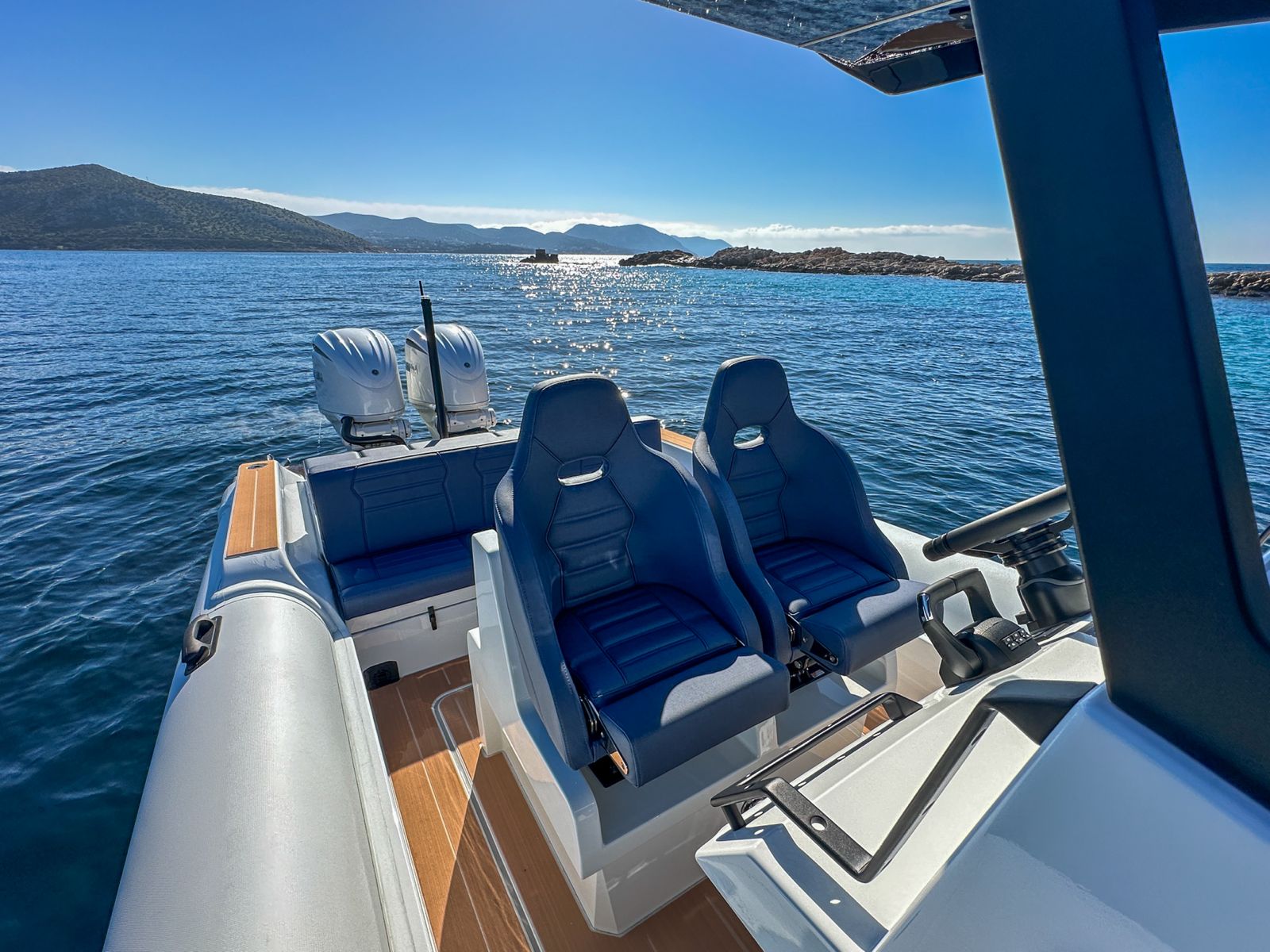 White Rock 36 speedboat with captain at helm cruising calm blue waters near Paros coastline with hills in background.
