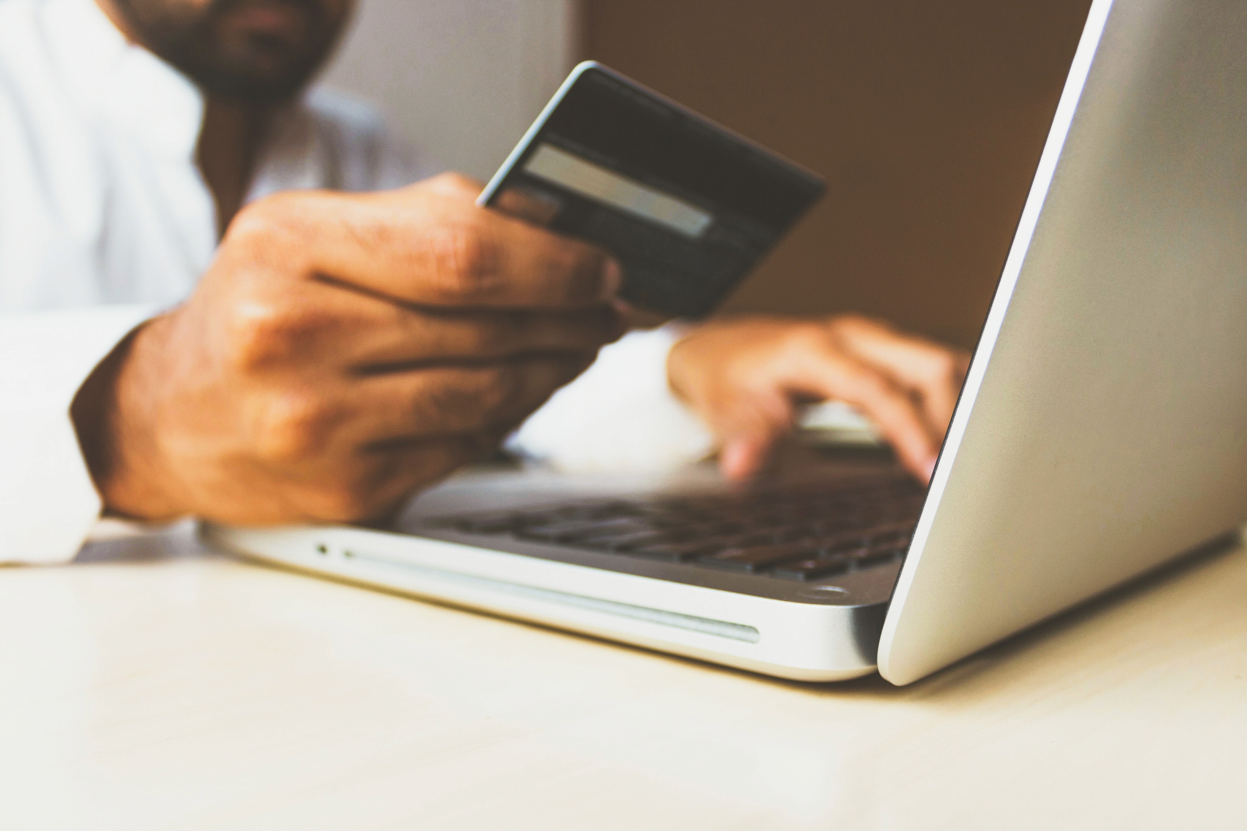 Pessoa fazendo compras online em frente a um computador com cartão de crédito em uma das mãos