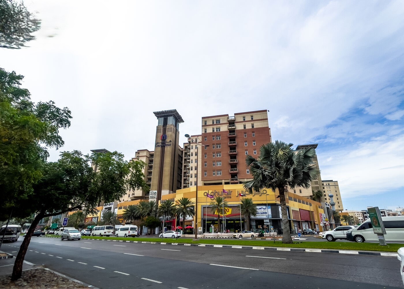 Busy street in Deira with palm trees, cars, and a multi-story building featuring shops below and residences above.