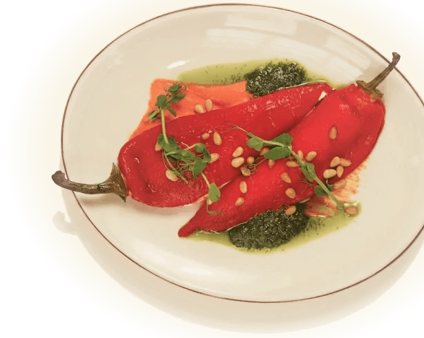 Roasted red peppers on a white plate with pesto, pine nuts, and microgreens.