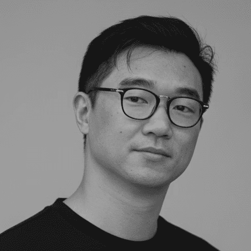 Portrait of a young man with short hair, wearing a dark t-shirt, against a plain background.