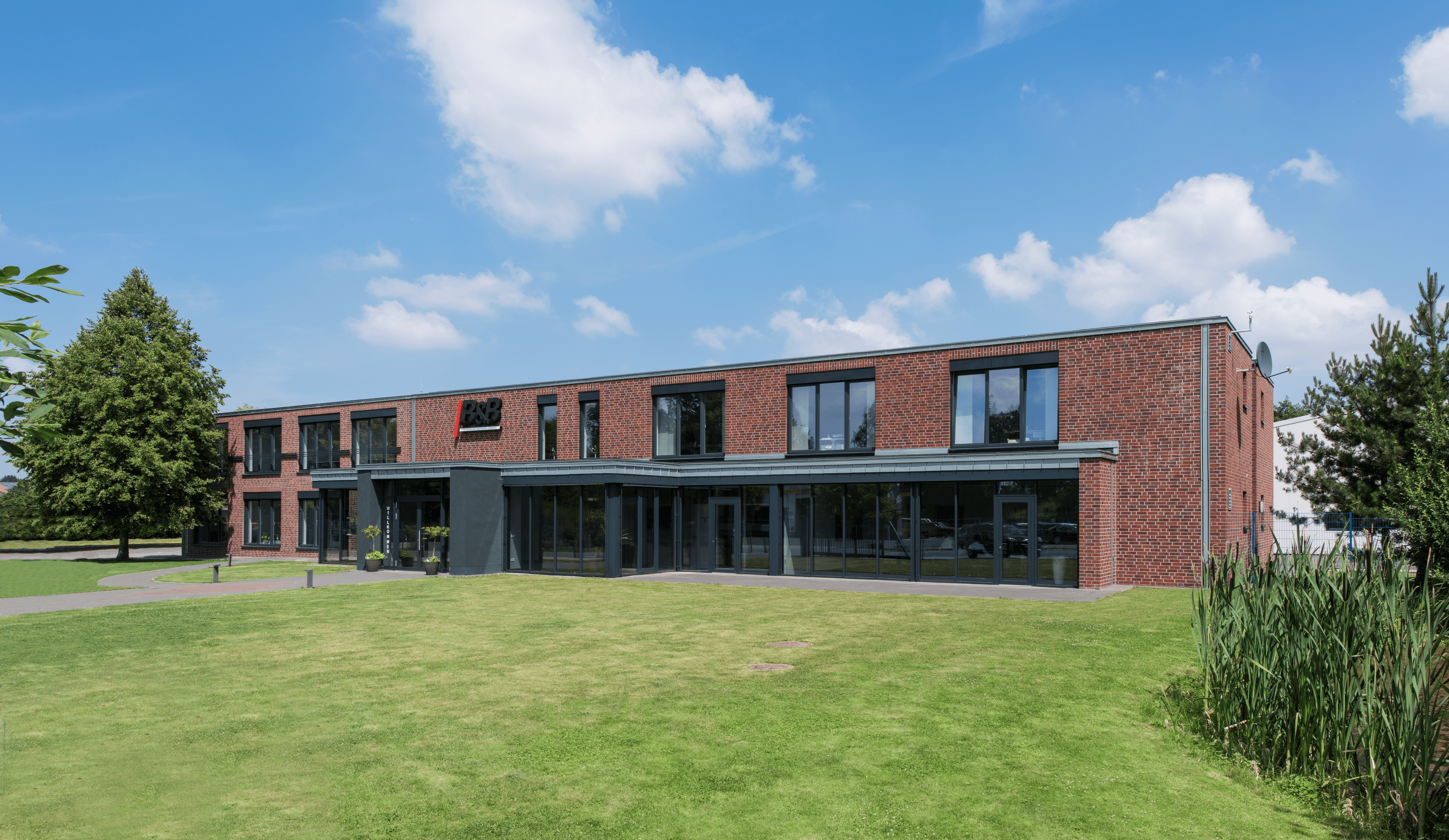 Modernes Backsteingebäude mit Glasfront & Rasenfläche. Architektur, Gewerbeimmobilie.