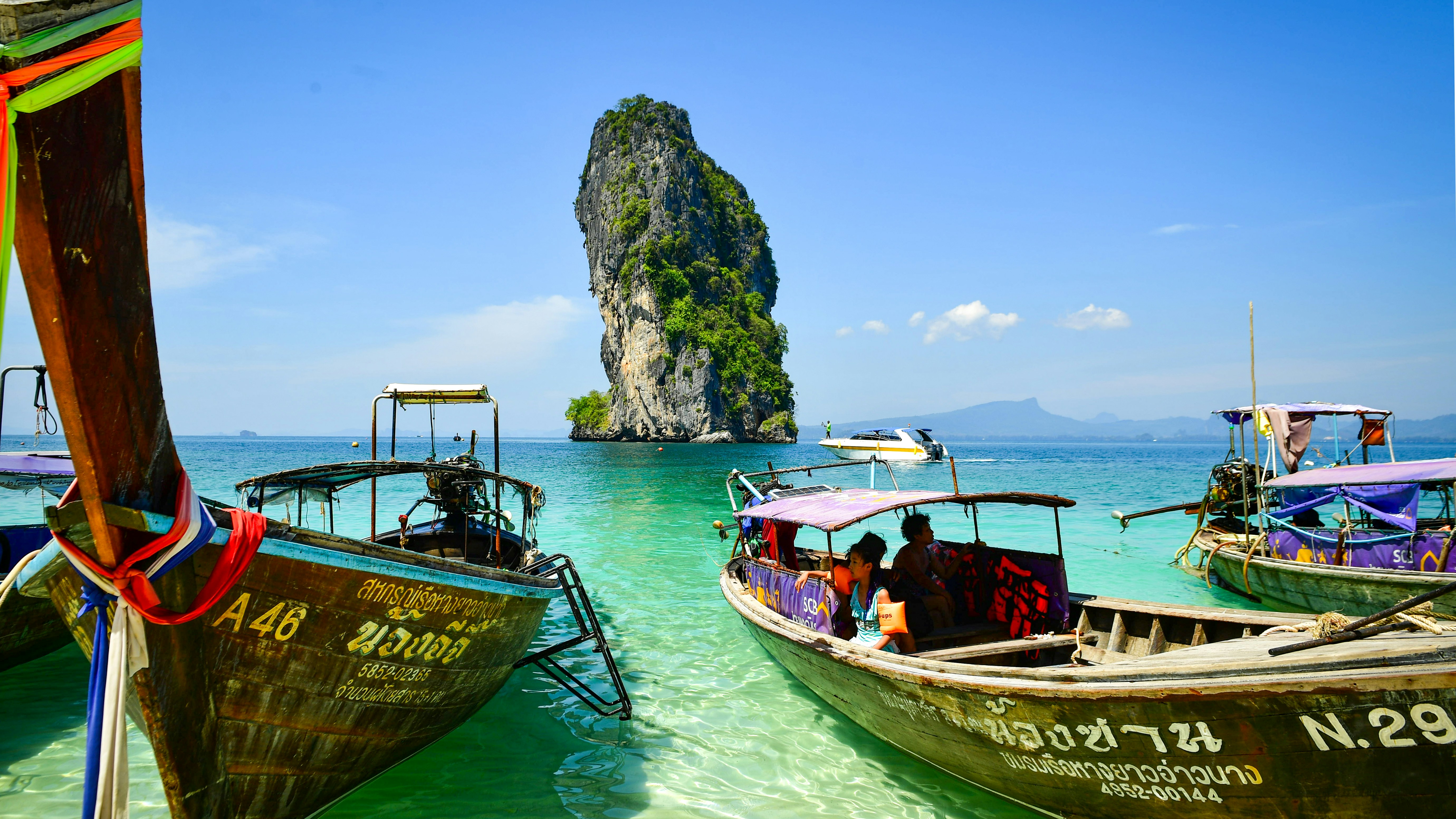 Longtail boats float in clear turquoise water near island.