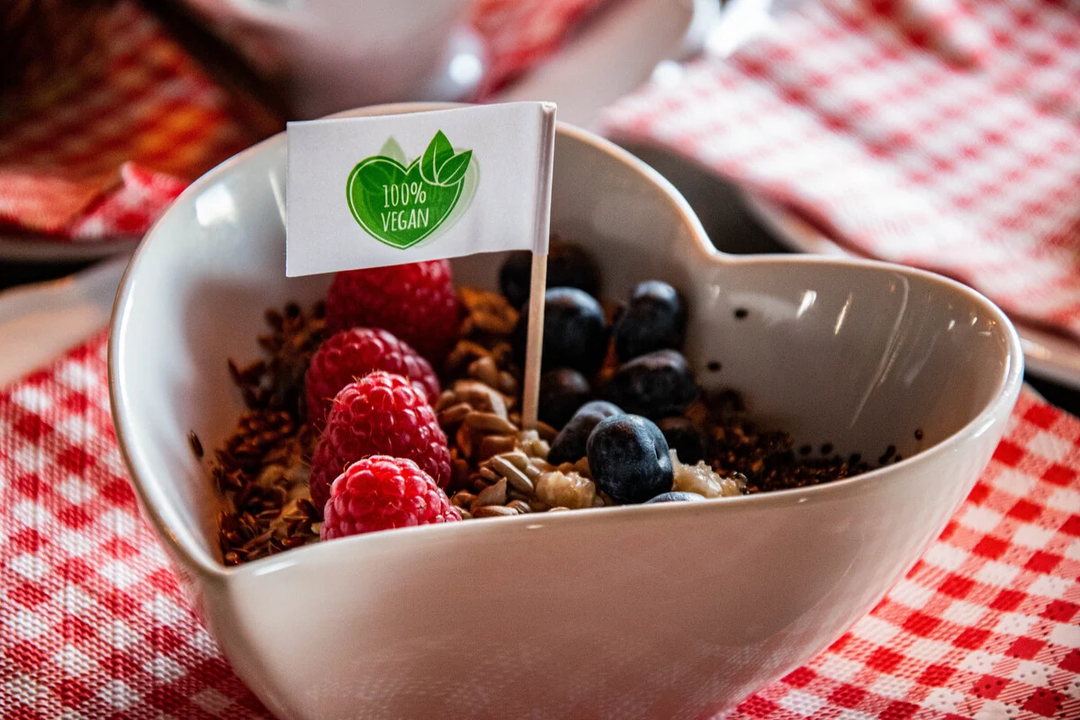 Ein Bild von einer Schüssel mit veganem Joghurt, Granola, Himbeeren und Blaubeeren,
