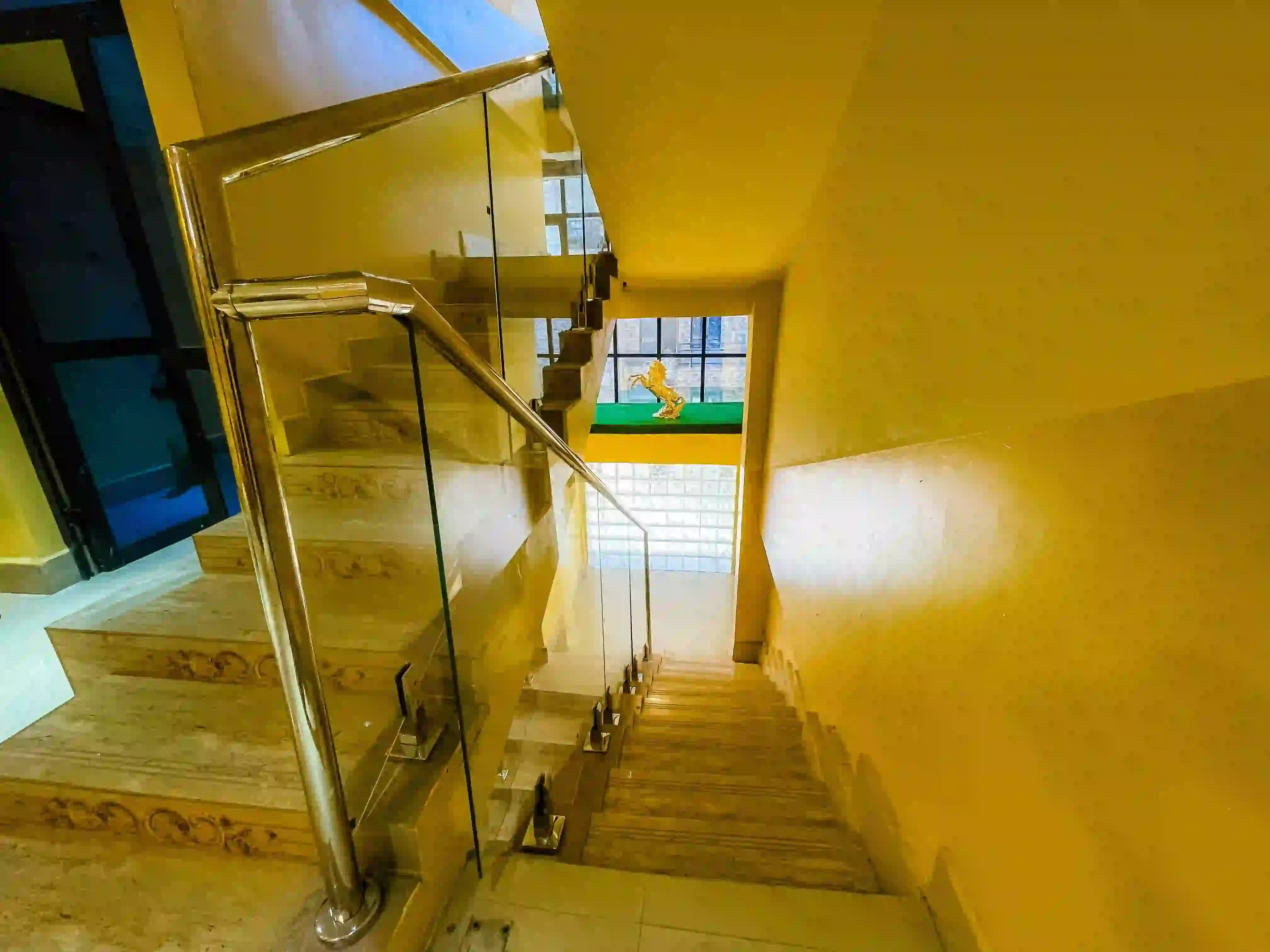 Escalier intérieur en pierre avec rampe vitrée et murs jaunes.