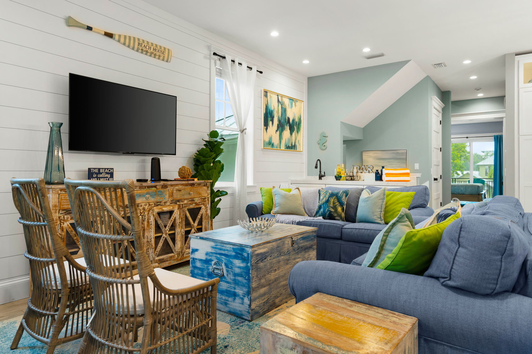 Coastal beach-themed living room with blue sofas, rattan chairs, a distressed blue trunk coffee table and a wall-mounted TV in an Anna Maria Island rental