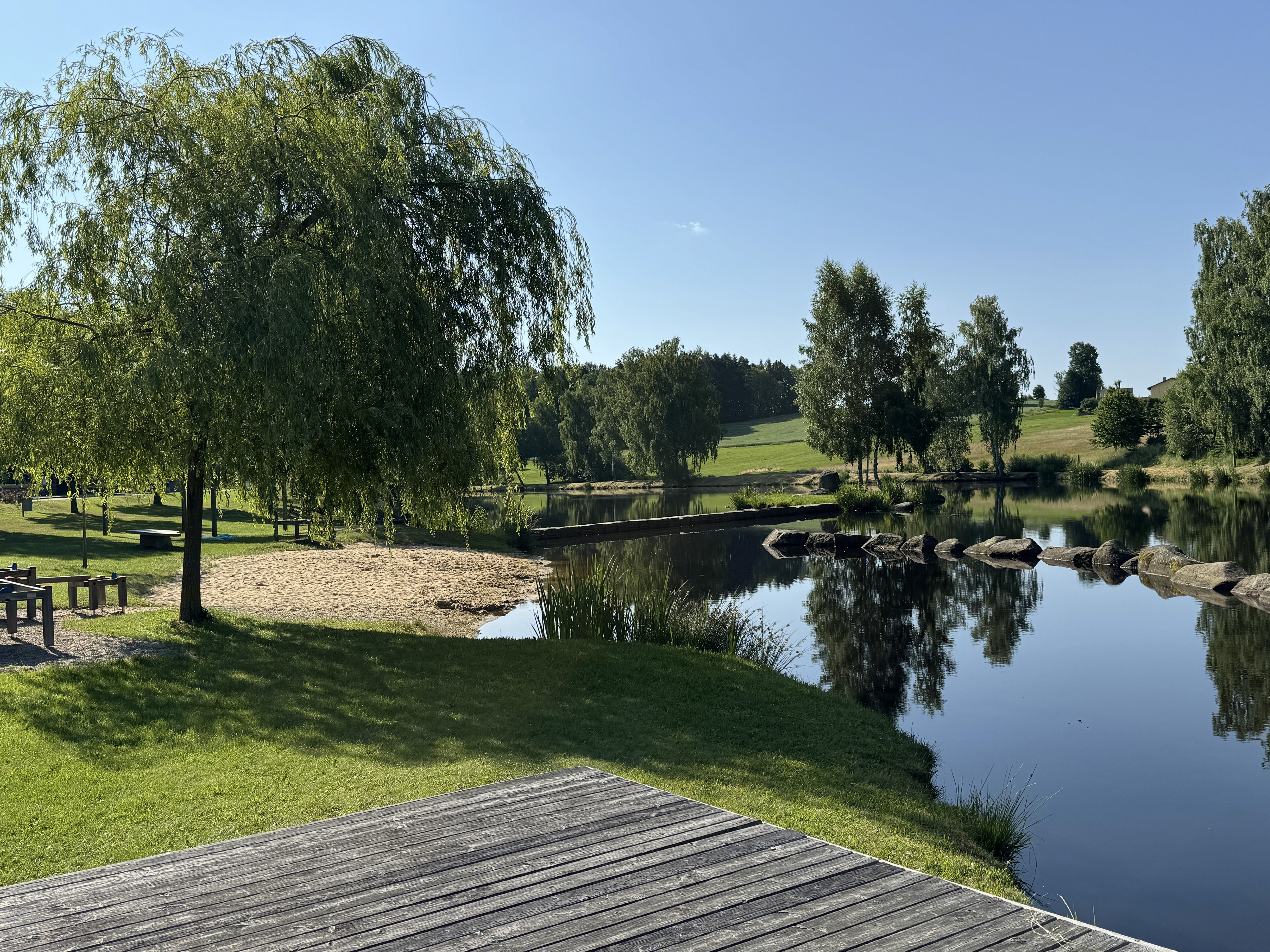 A serene lake reflects clear blue skies and green trees on a sunny day.
