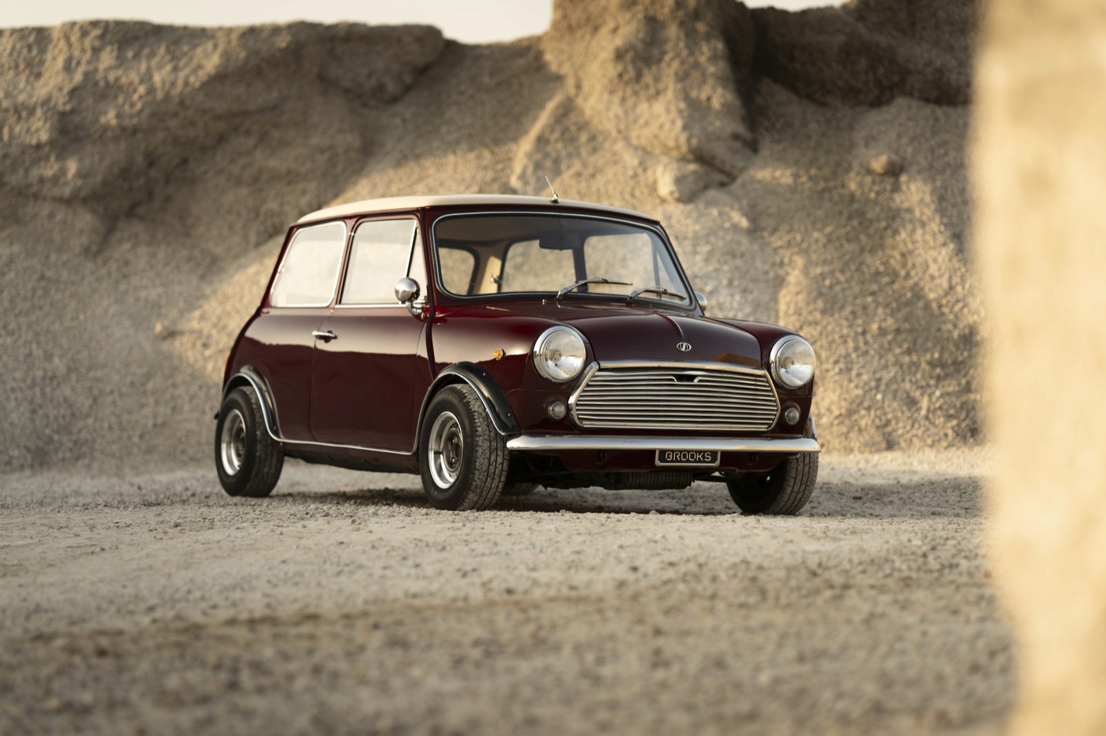 A vintage mini classic parked on a rocky surface with a rock landscape in the background. Warm lighting enhances the scene.