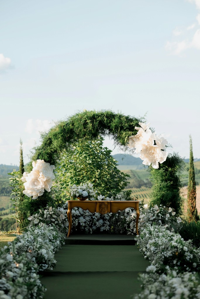 Circular greenery wedding arch with oversized white peonies and a vintage gold table overlooking rolling hills and cypress trees