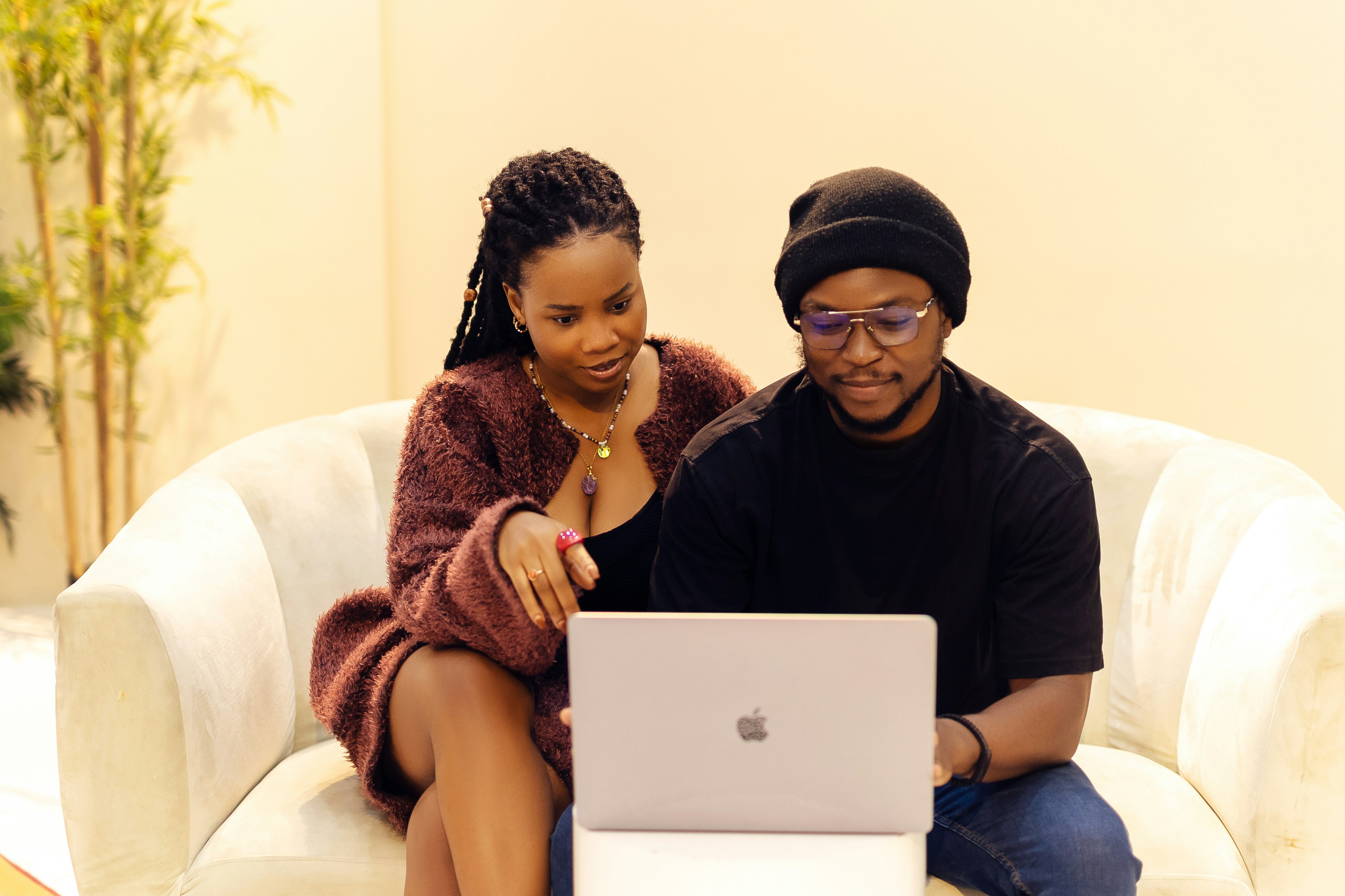 A man and a woman sitting on a couch looking at a laptop