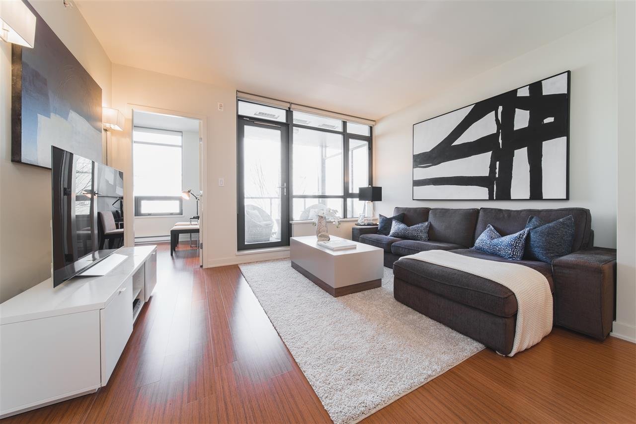 Modern living room with a couch, TV, and large windows, featuring wooden flooring and minimalist decor.