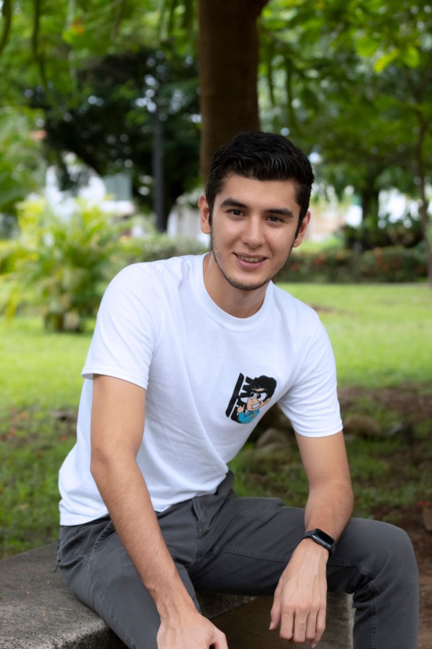 A young person with long, wavy hair sits in front of a plain background, looking directly at the camera.
