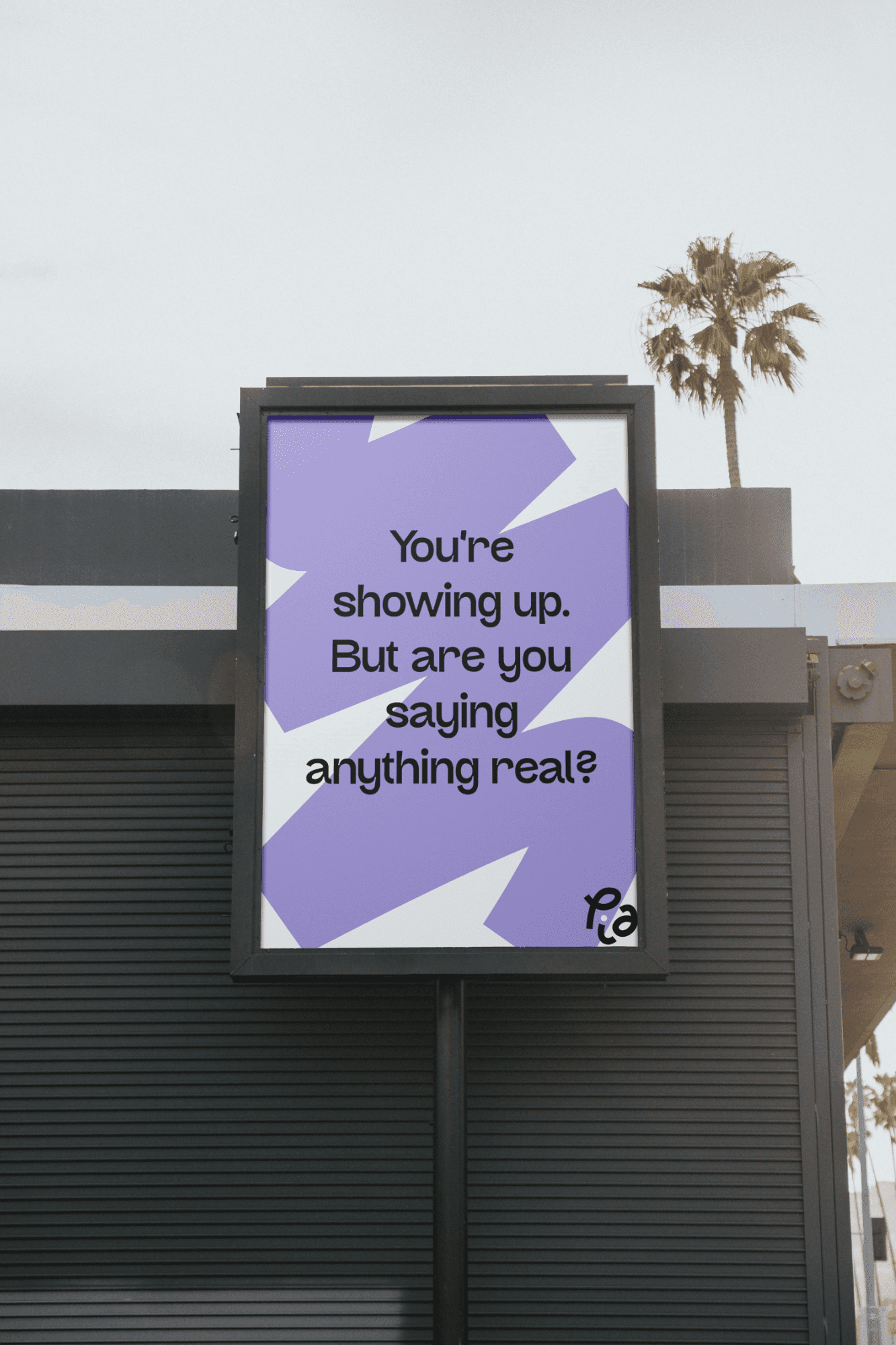 A purple and white abstract geometric billboard displays the message "You're showing up. But are you saying anything real?" against a gray wall, with a palm tree and clear sky in the background.