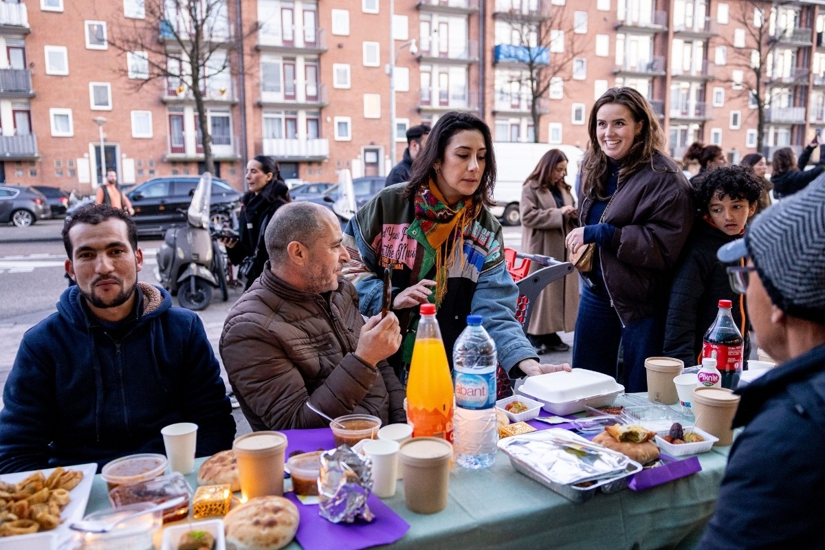 Buurtbewoners eten samen aan een lange tafel op straat