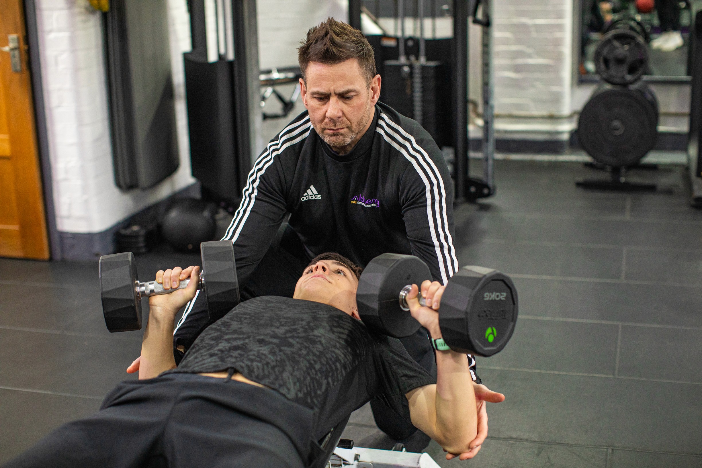 Personal trainer acting as spotter for a young man lifting weights to gain muscular strength.