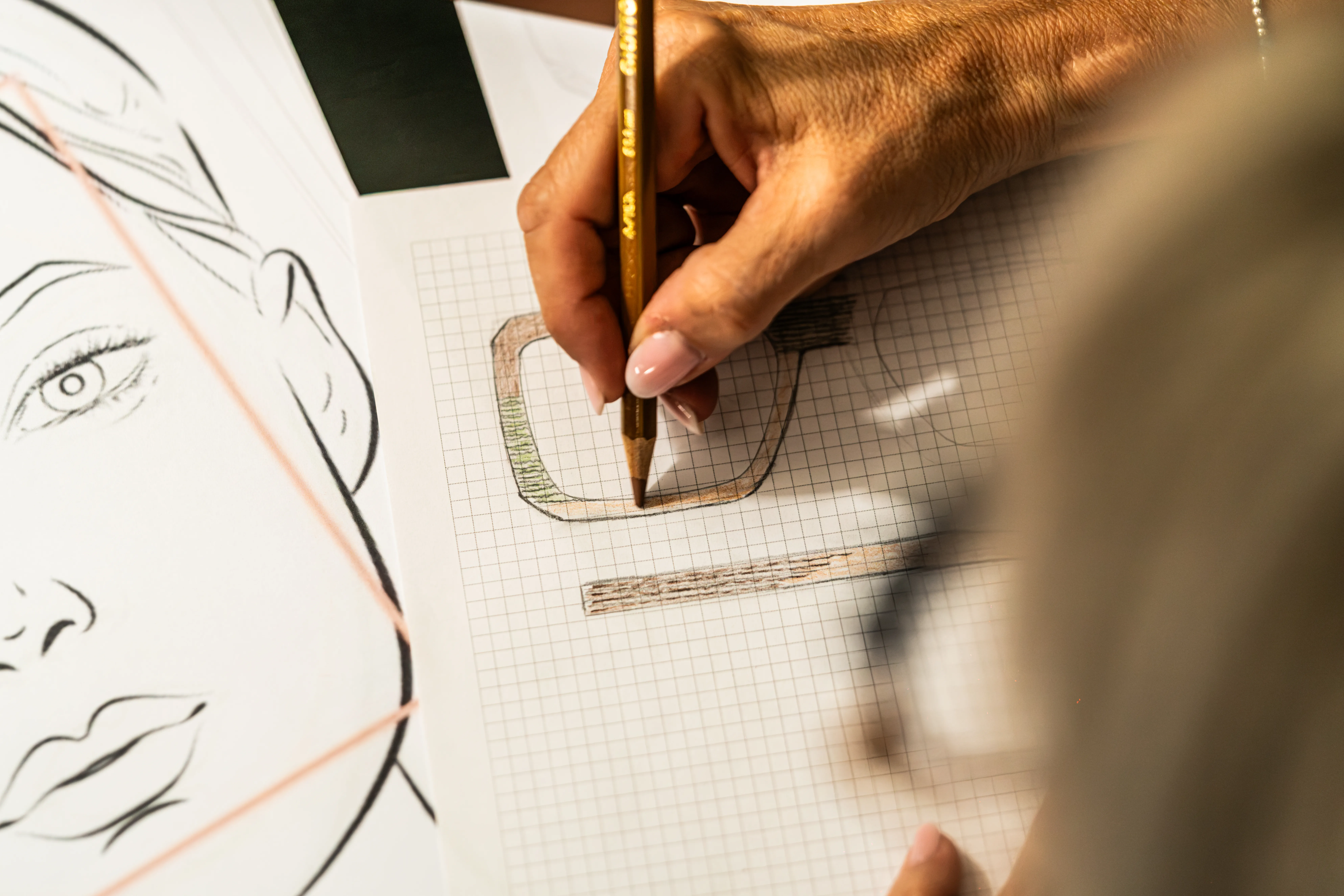 Progettazione manuale di un occhiale IDIA su misura di Ottica Dentella ad Ancona, con una mano che disegna la forma della montatura su carta millimetrata partendo da misure, proporzioni e caratteristiche individuali. IDIA è il progetto di eyewear personalizzato di Ottica Dentella in cui ogni occhiale nasce dalla persona, dallo studio del viso, dei lineamenti, dei colori e delle esigenze estetiche e visive, per creare una montatura unica progettata e realizzata su misura.
