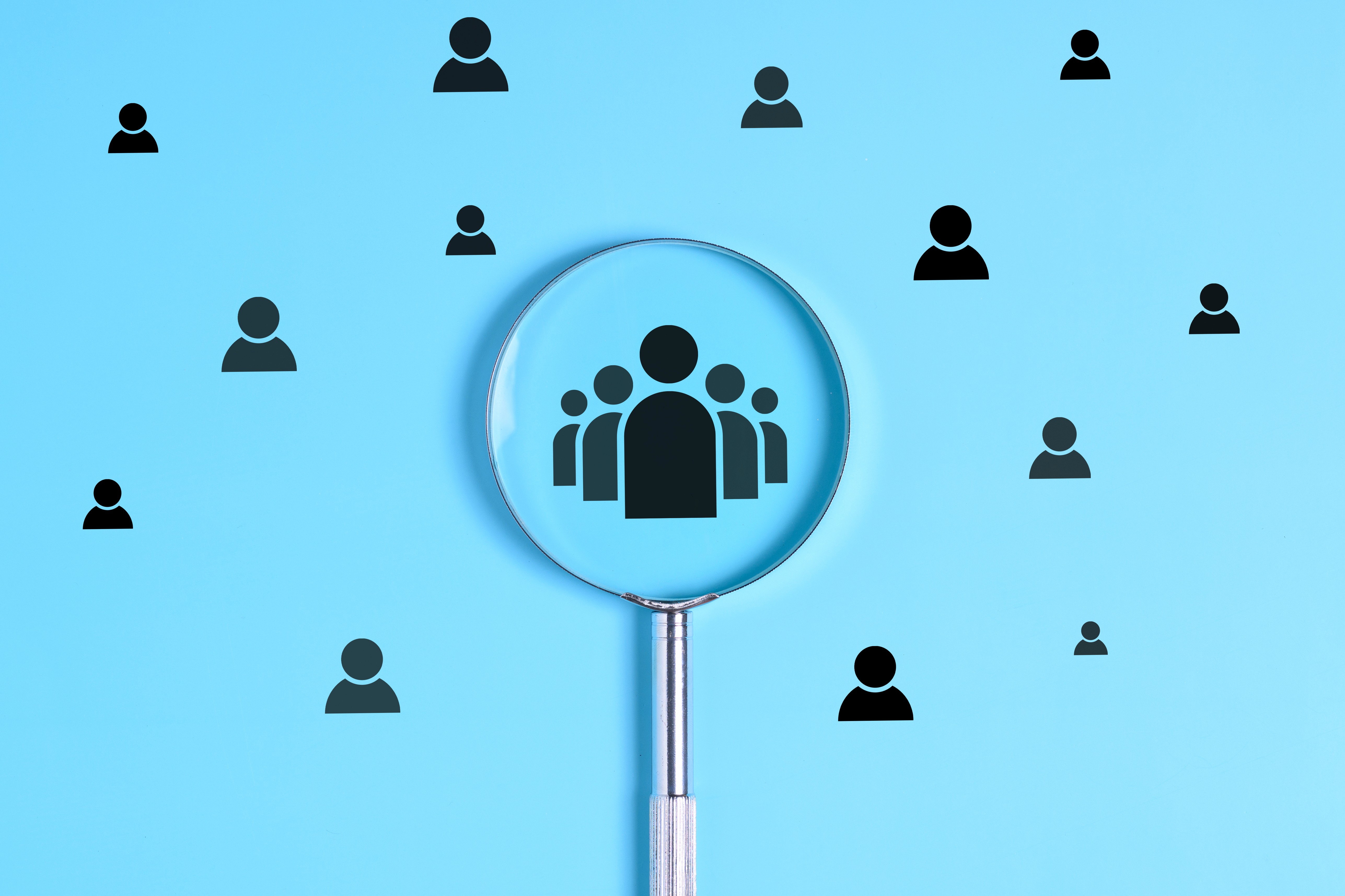 Magnifying glass focusing on a group of people icons surrounded by individual figures on a blue background, representing how AI search systems identify and surface the most authoritative voices in a market when answering buyer questions