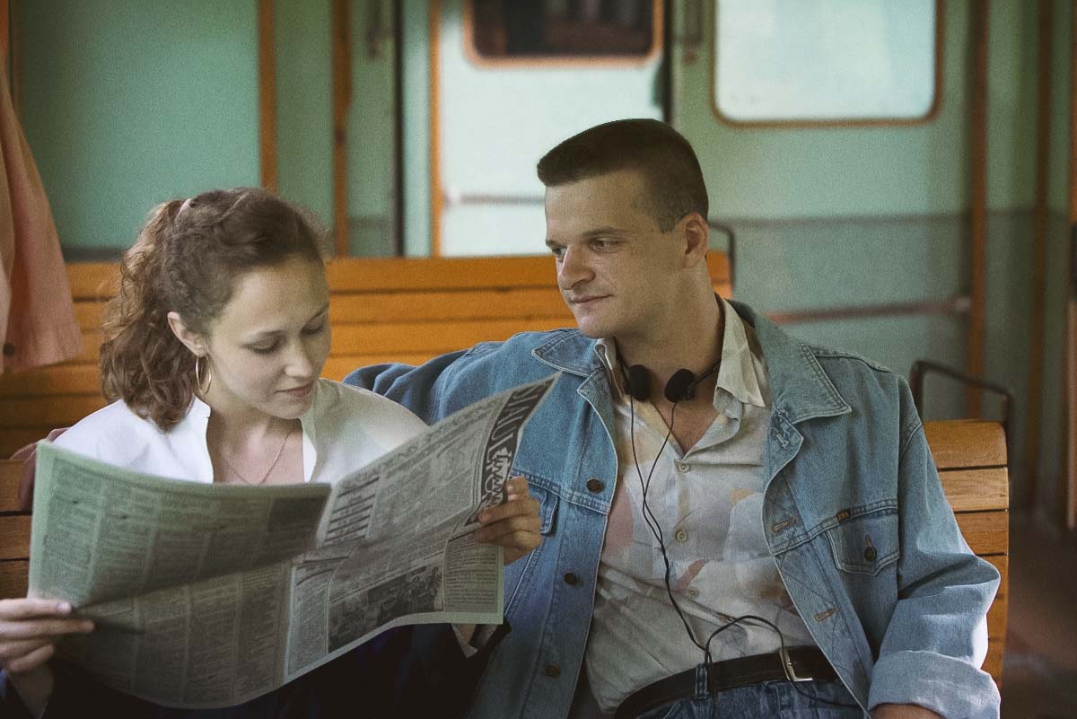 Rimants (Džiugas Grinys) and Monika (Digna Kulionytė) laughing together in the train, capturing young love in the Baltic 90s coming-of-age film Southern Chronicles.