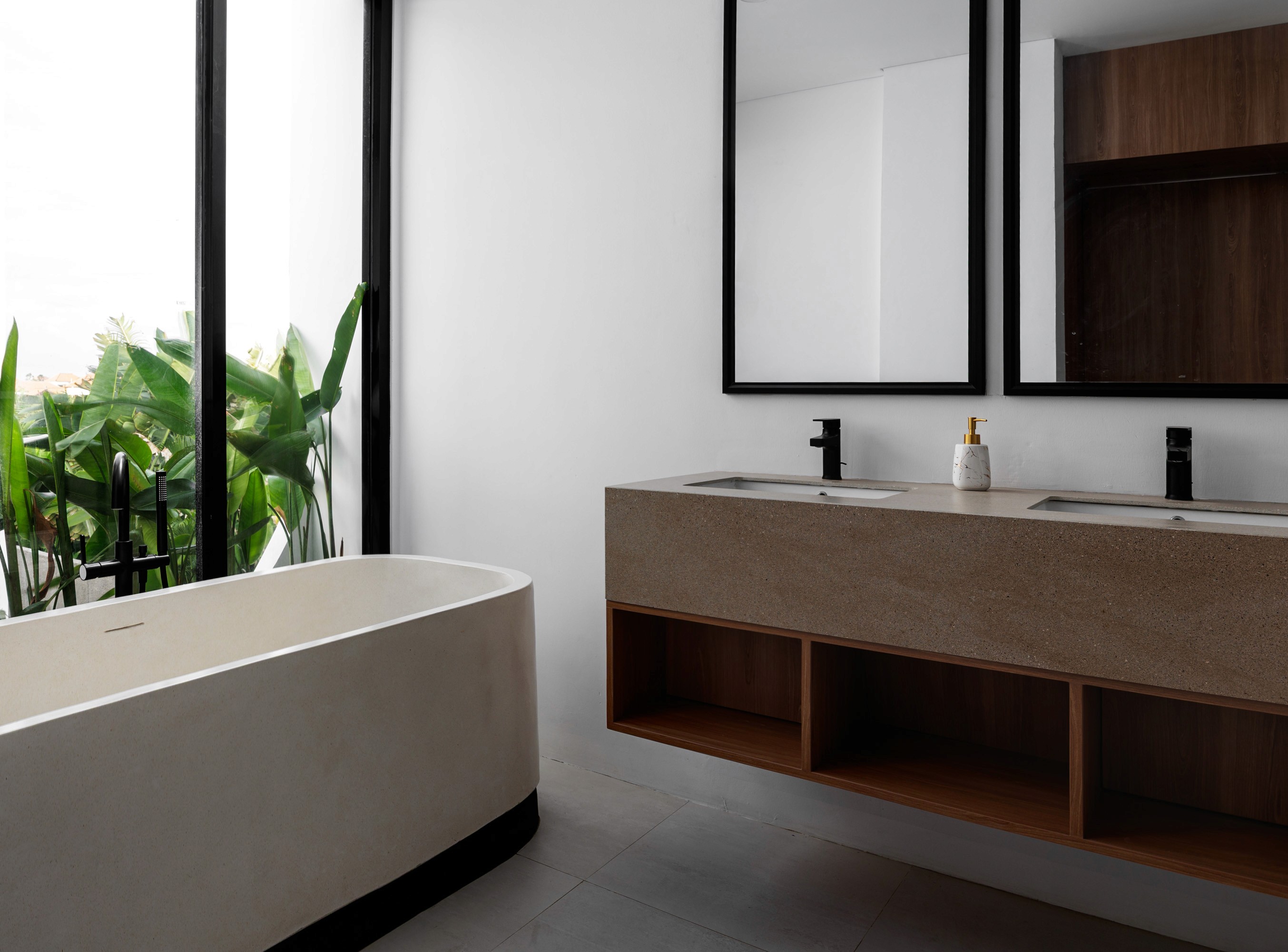 Freestanding bathtub beside large glass window, floating double vanity with black fixtures, and full-height mirrors reflecting wood cabinet.