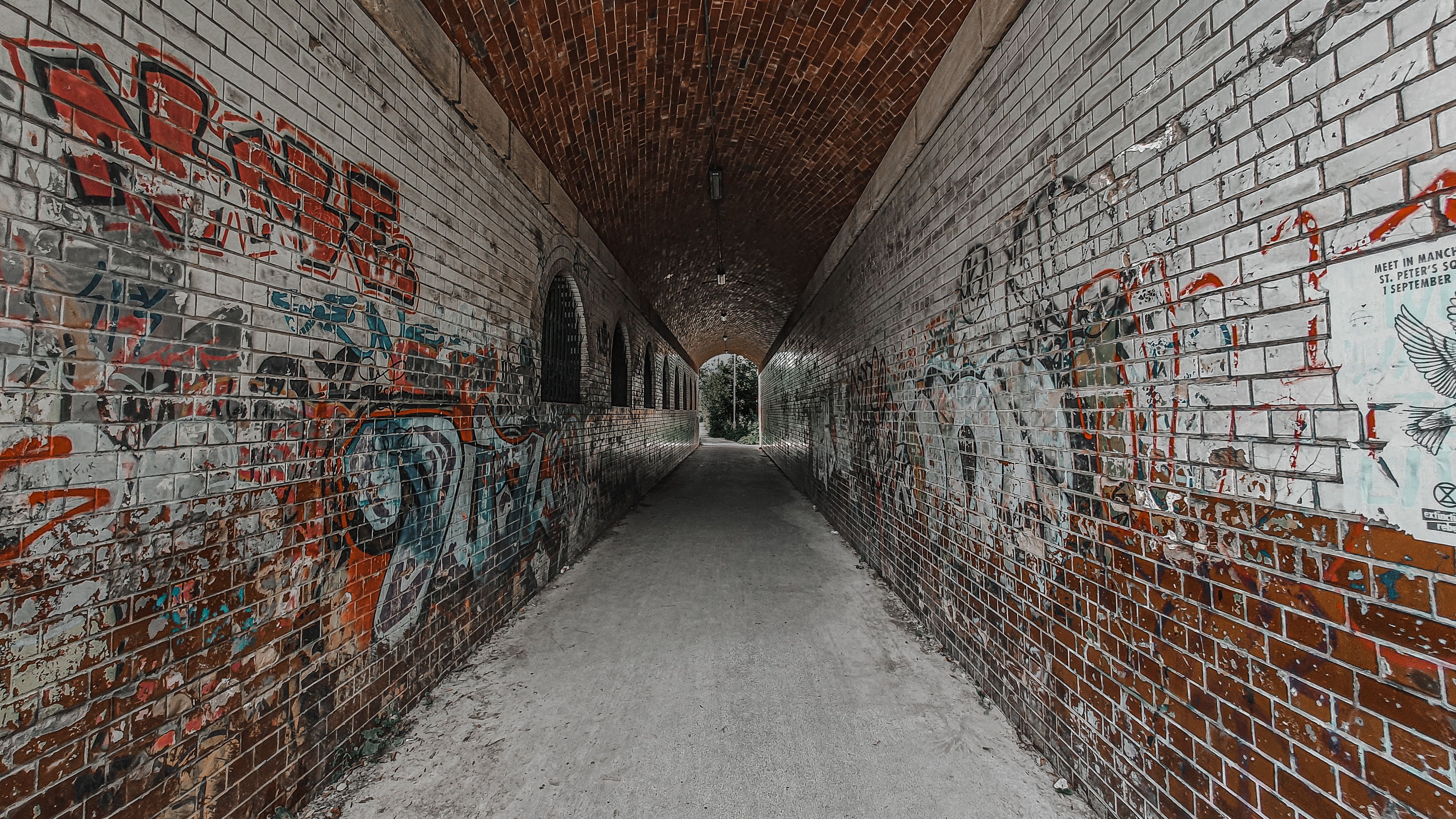 A dimly lit corridor featuring brick walls with peeling paint and graffiti, leading to an indistinct end.