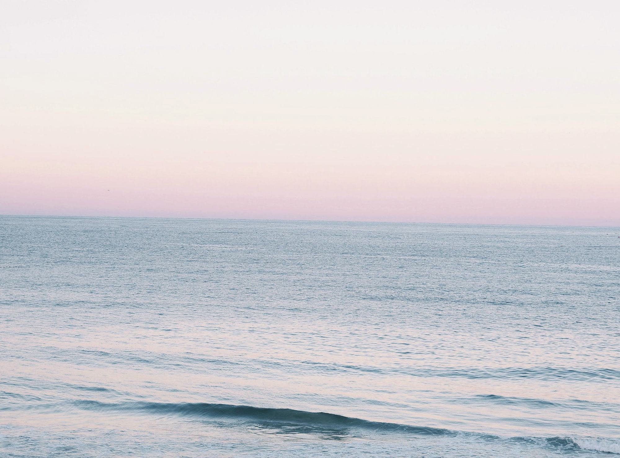 A calm sea under a pink and lilac sky just before sunrise